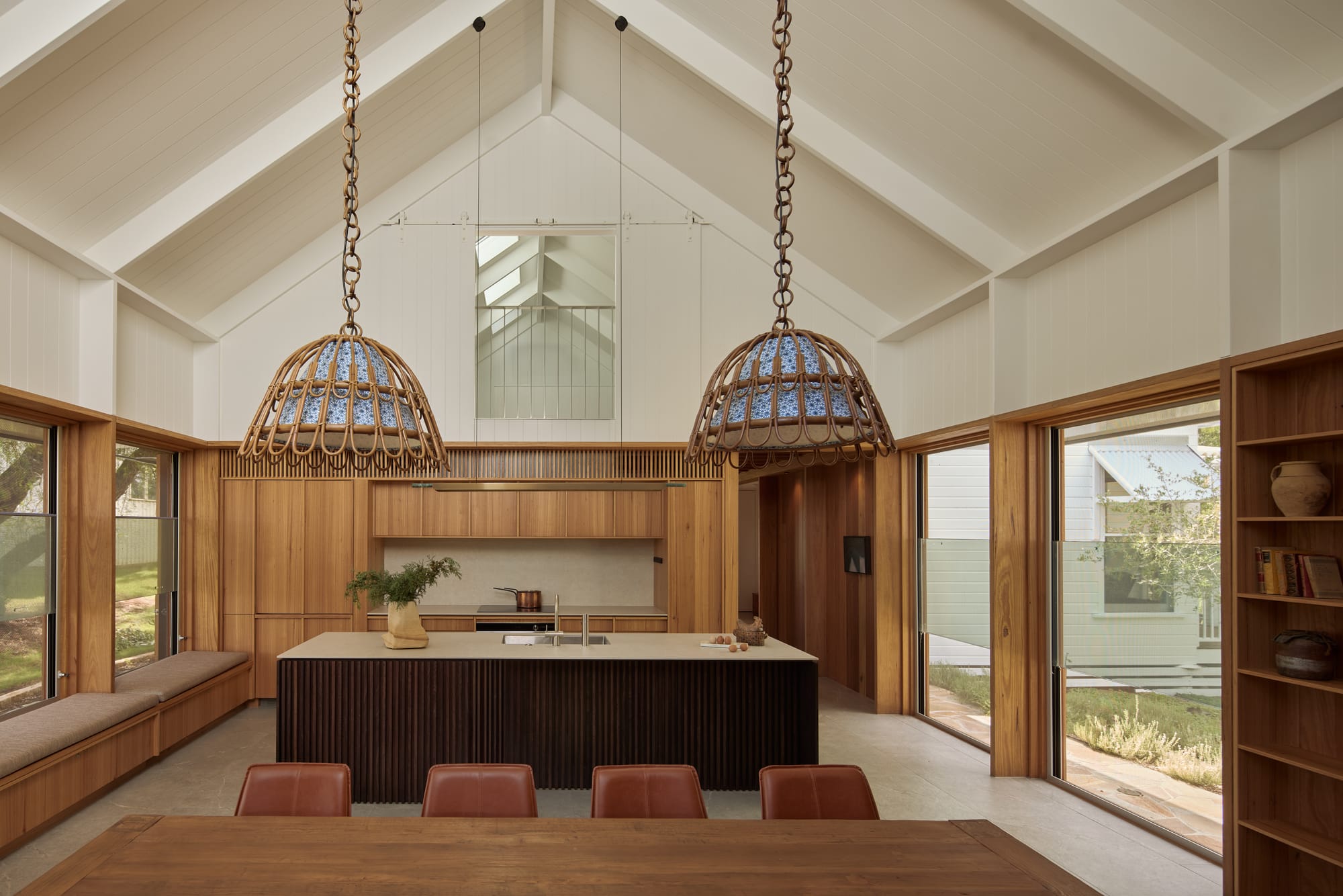 Binnum Homestead by Alexandra Buchanan Architecture. Photography by Cieran Murphy. Open plan kitchen and dining area with A-frame with exposed ceiling, large pendant lights over a timber dining table and timber kitchen joinery. 