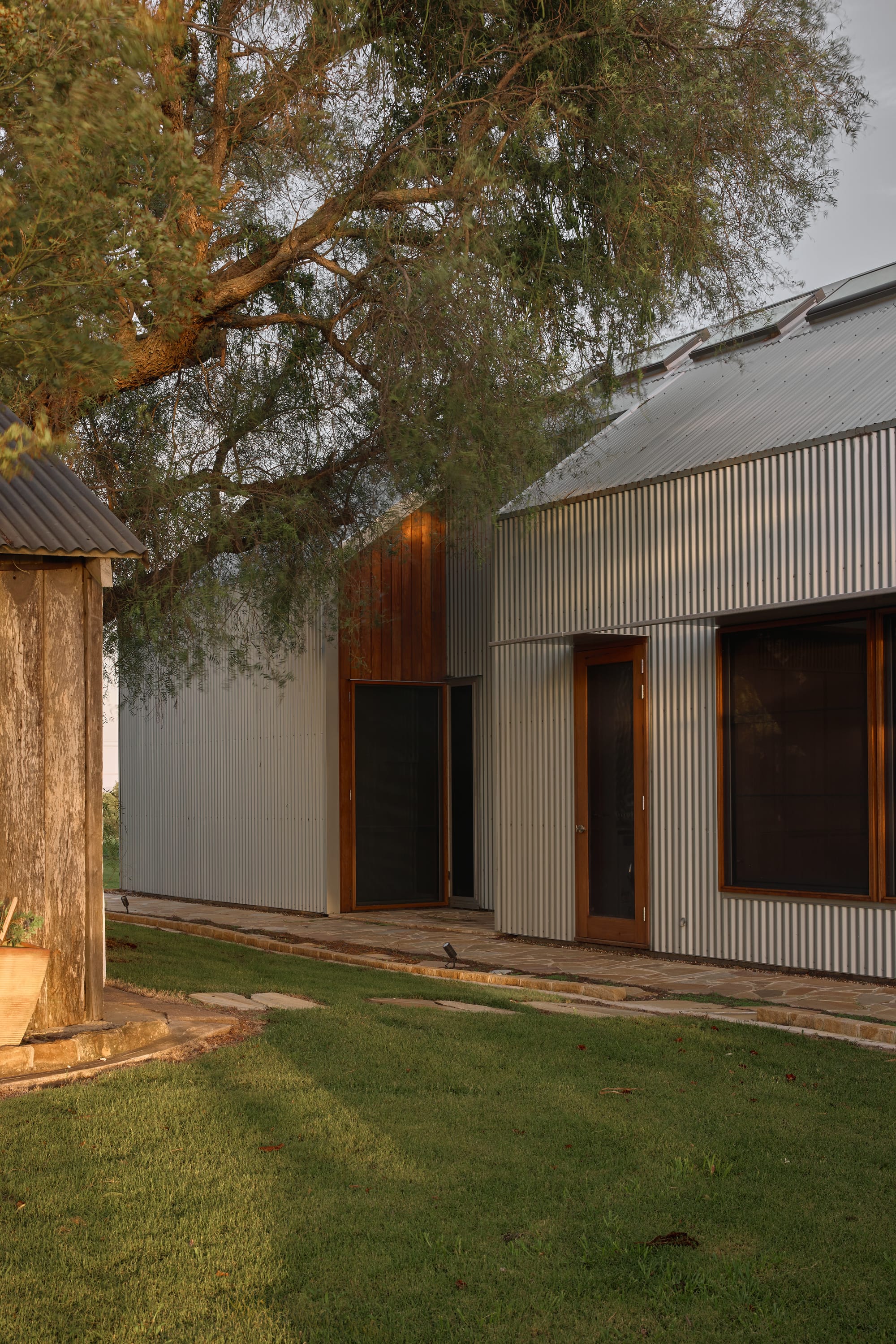 Binnum Homestead by Alexandra Buchanan Architecture. Photography by Cieran Murphy. Facade of home clad in corrugated iron, with timber doors and windows, and sandstone paver patio. 