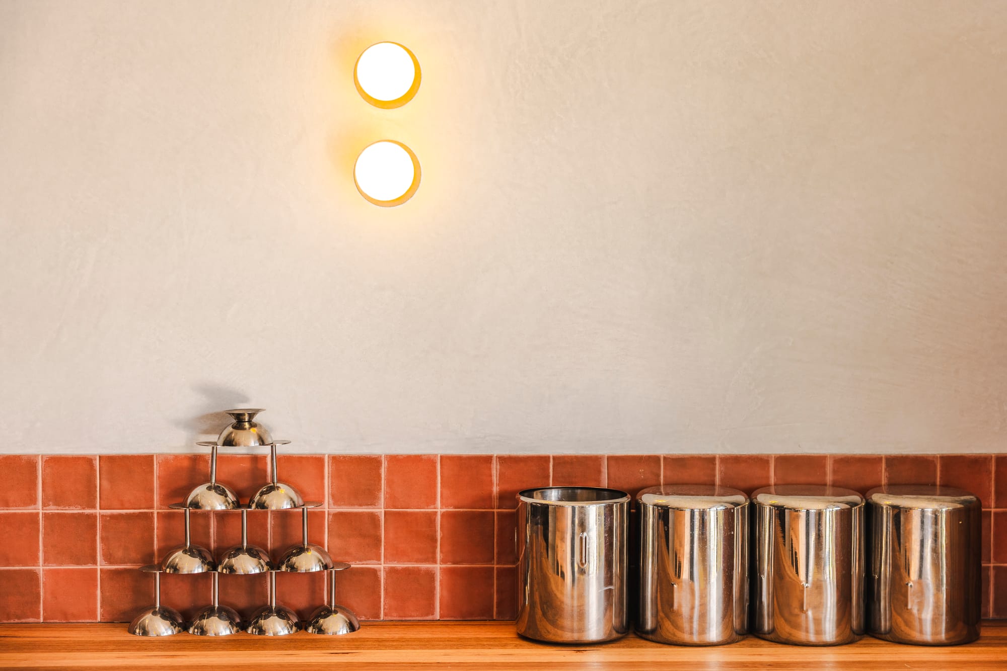 The Cafe by Bel.Bon Design. Photography by Sana Brotherson. Timber countertop, terracotta tiled splashback, white walls and chrome storage tubs and icecream bowls. 