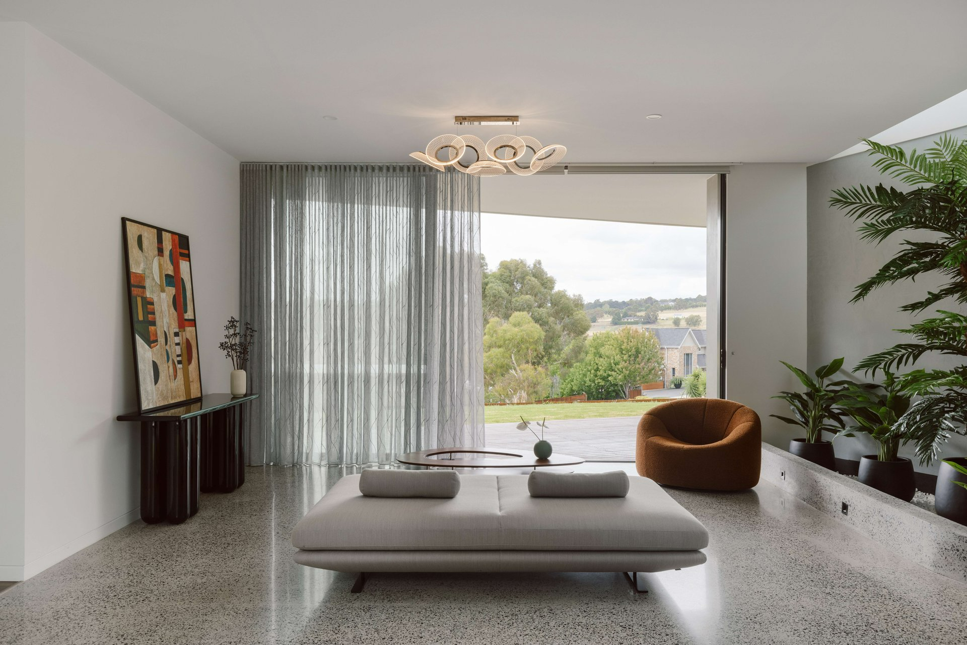 House on the Hill by ENCLAVE Architects. Photography by Elise Scott. Living space with flat, grey couch, full heigh grey sheers in front of wall-length window and large potted plants on left hand side. 