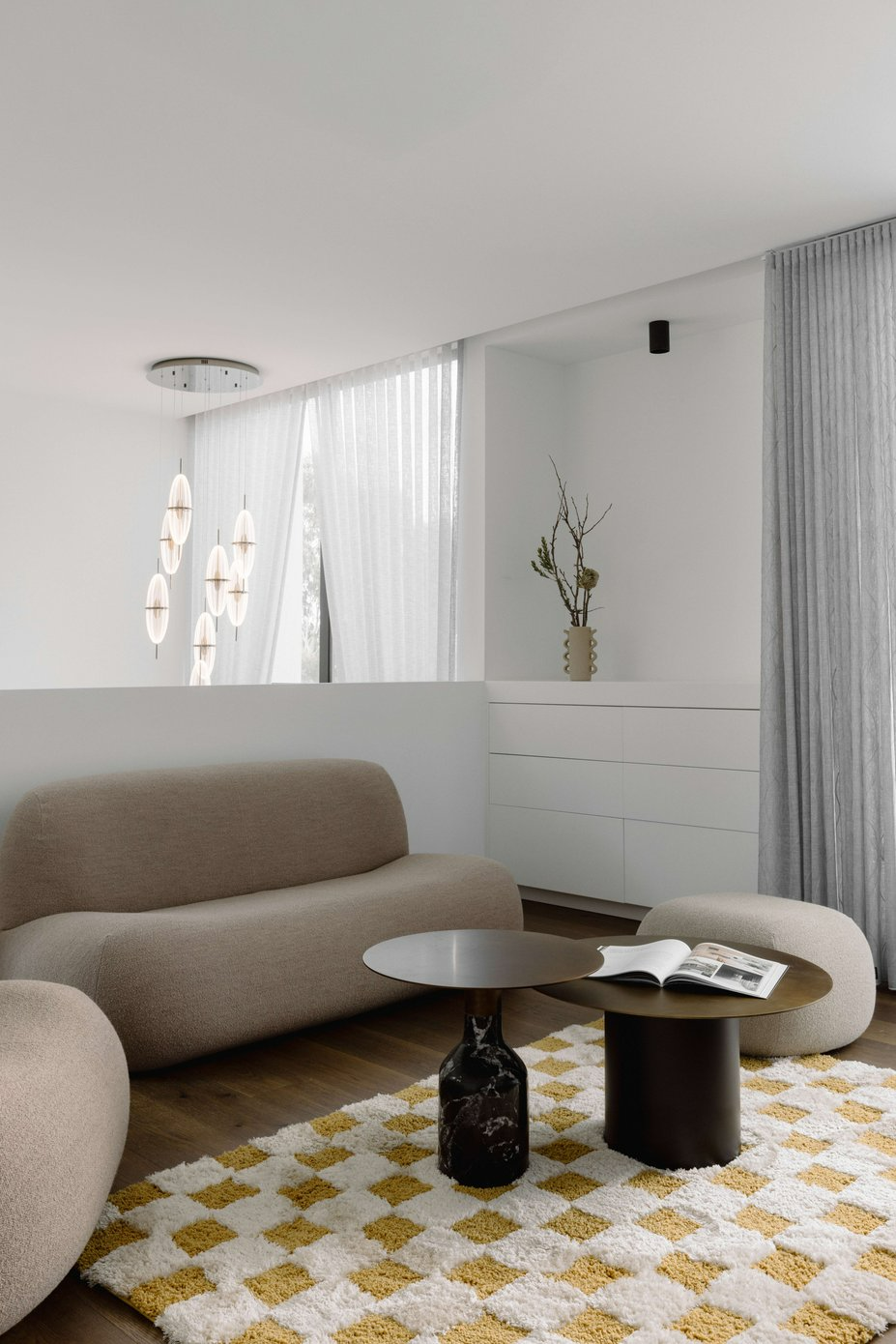 House on the Hill by ENCLAVE Architects. Photography by Elise Scott. Living space with organically shaped beige couch, black round coffee tables and yellow and white checkerboard floor rug. 