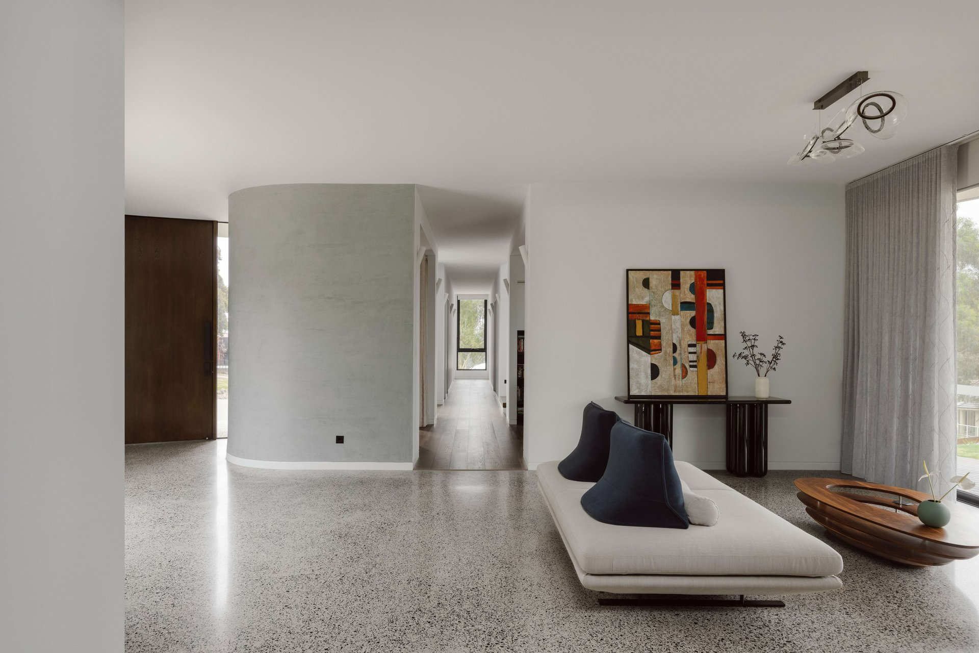 House on the Hill by ENCLAVE Architects. Photography by Elise Scott. Expansive, open plan entry with polished concrete flooring, white curved walls, an abstract white and navy couch, and long hallway with timber floors. 