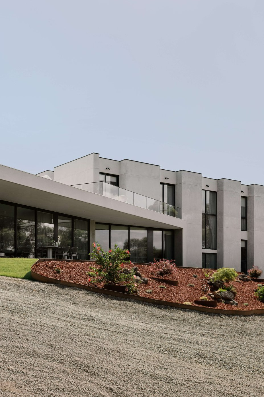 House on the Hill by ENCLAVE Architects. Photography by Elise Scott. Large, contemporary concrete home sat atop hill, with large balcony, landscapes garden beds and windows across ground floor. 