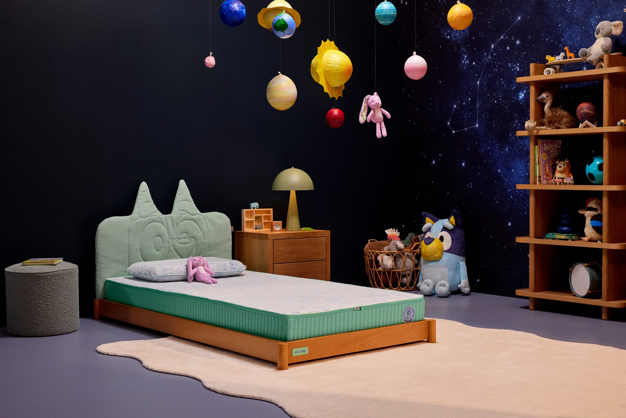 Koala x Bluey Snoozytime Bed Frame by Koala. Timber bed frame with teal fabric headboard with ears, in room with dark, space-inspired walls and decorations. 