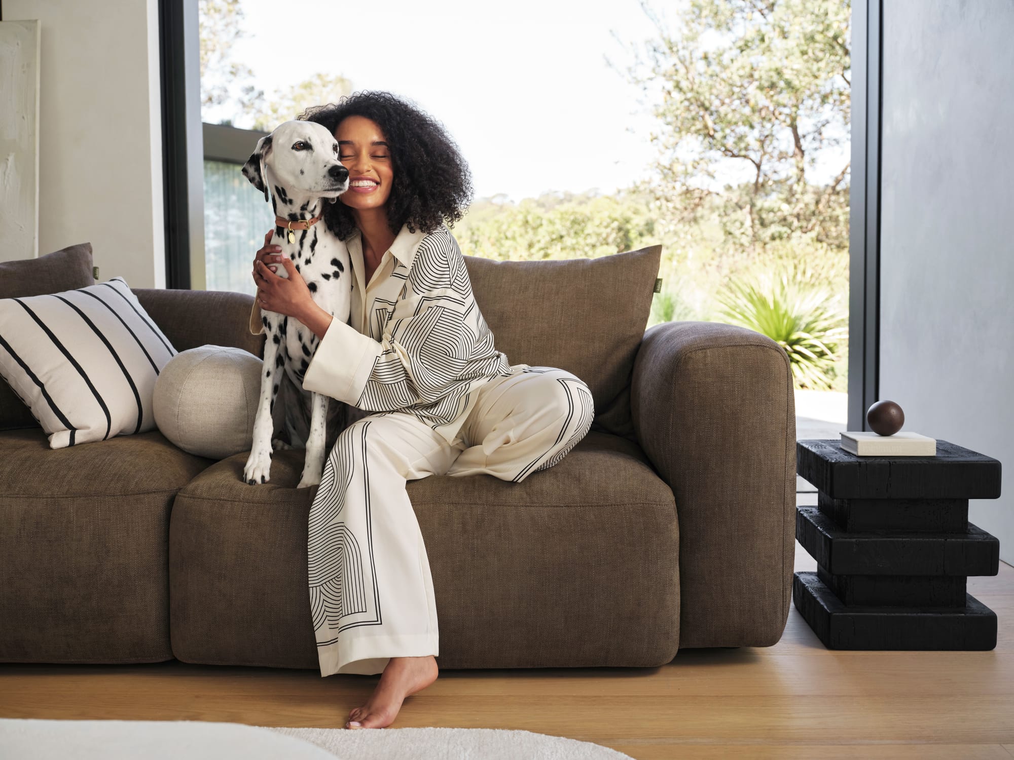 Torquay Sofa in Midnight Mocha by Koala. Woman sitting on brown couch, hugging a Dalmation.
