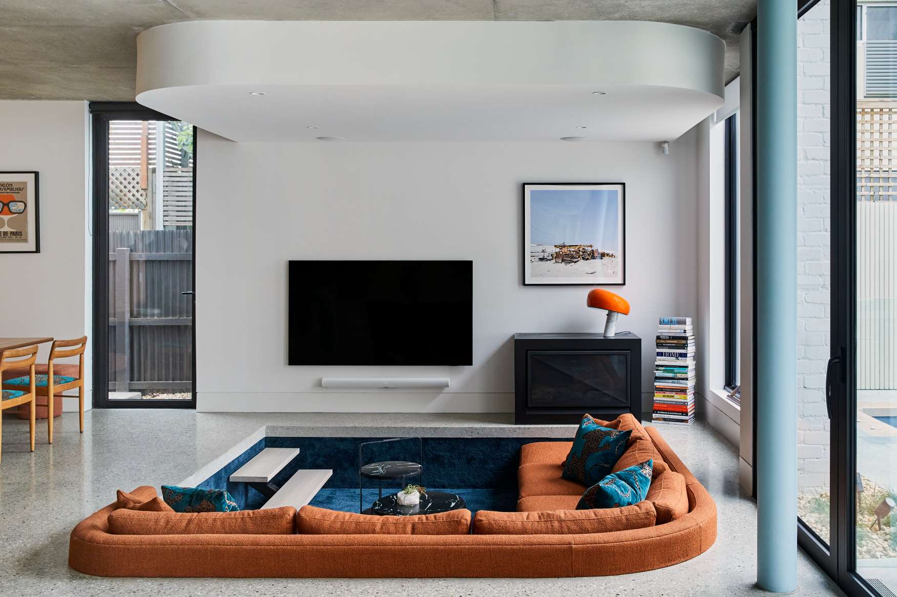 Park St by SGKS ARCH. Photography by Tania Lee. Living space with sunken orange lounge with navy blue carpet, curved bulkhead and light blue pillar. 