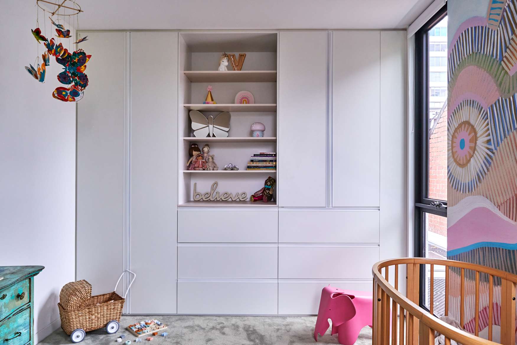 Park St by SGKS ARCH. Photography by Tania Lee. Nursery with full-height joinery and storage, grey carpet and colourful, patterned wallpaper above timber crib. 