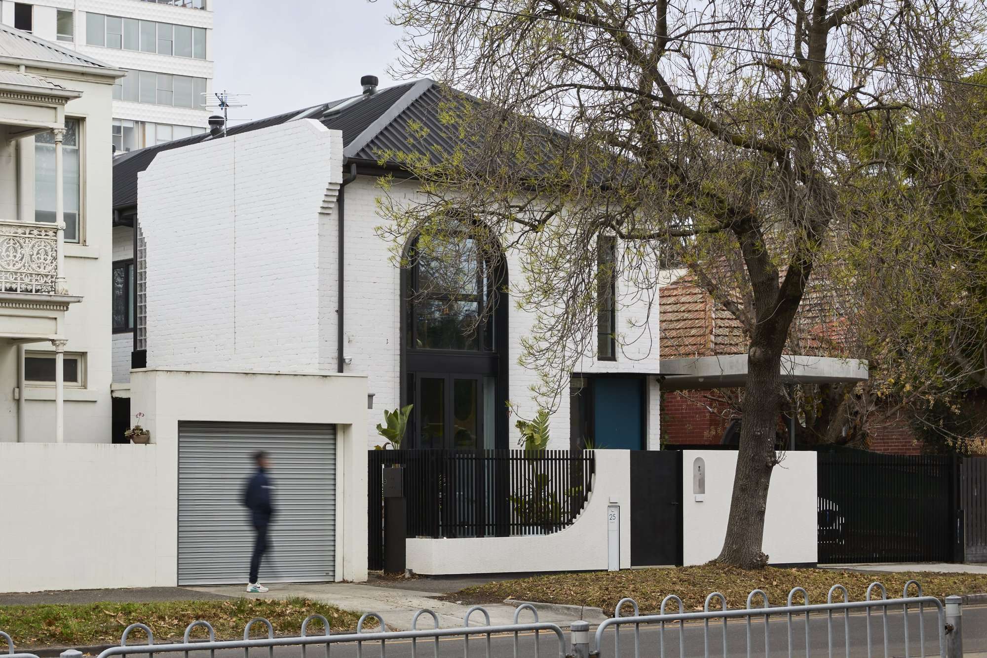 Park St by SGKS ARCH. Photography by Tania Lee. Double storey white brick terrace home with double storey black arched doorway and window and teal front door. 