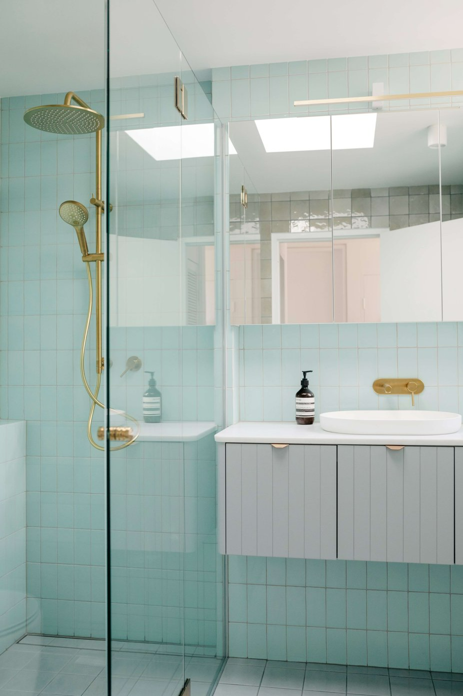 Westleigh Wonder by Nathalie Scipioni Architects. Photography by Alexandra Adoncello. Aquamarine bathroom with tiled floors and walls, grey timber clad vanity and gold fixtures. 