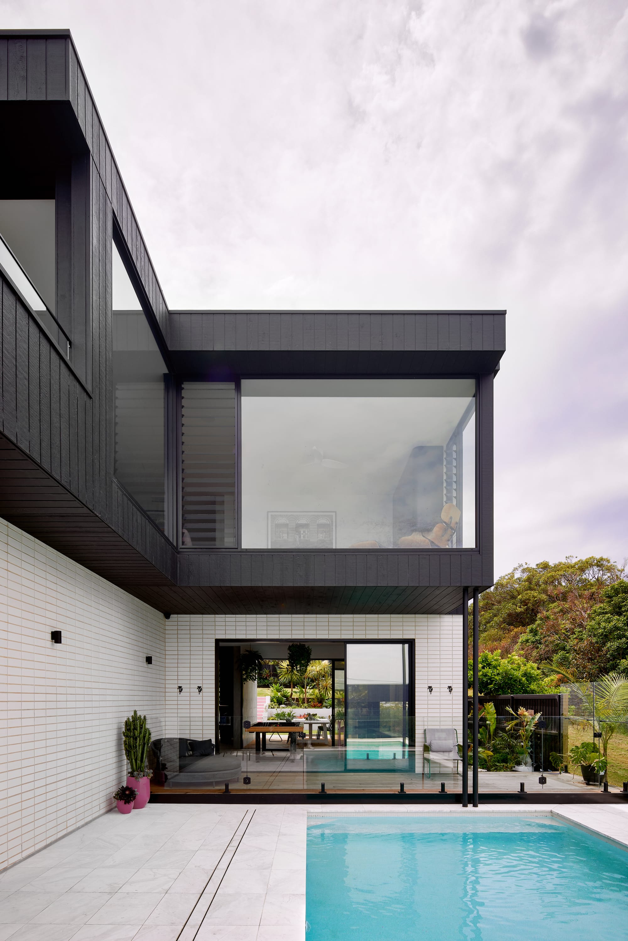 Headland House by Baikie Corr Architecture. Photography by Toby Peet. Rear facade of double storey home with white brick and black timber clad exterior, a pool and timber deck. 