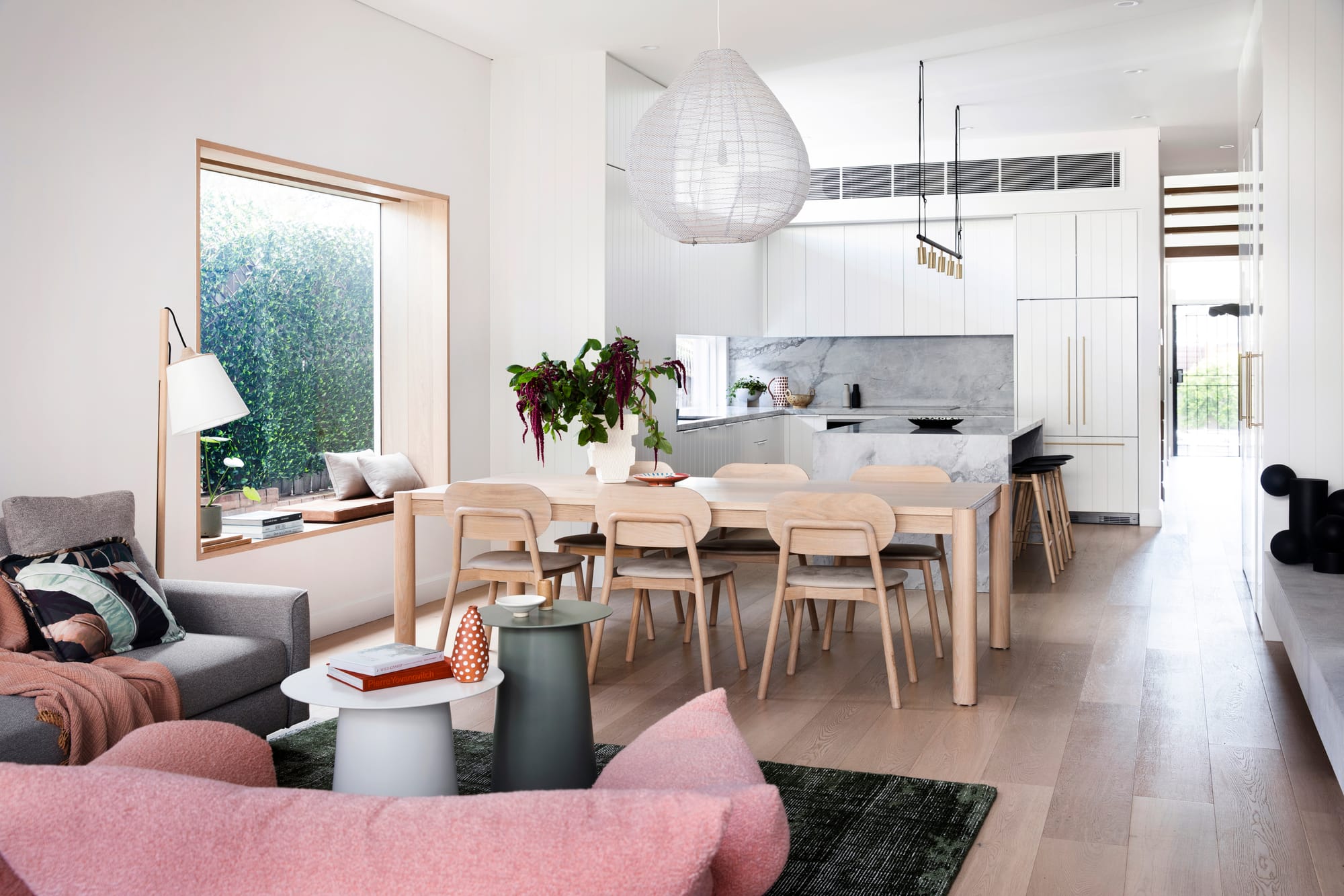 Bondi Beach House by Baikie Corr Architecture. Photography by Chris Warnes. Open plan living, dining and kitchen with timer floors, white walls, a timber dining table and a pink couch. 