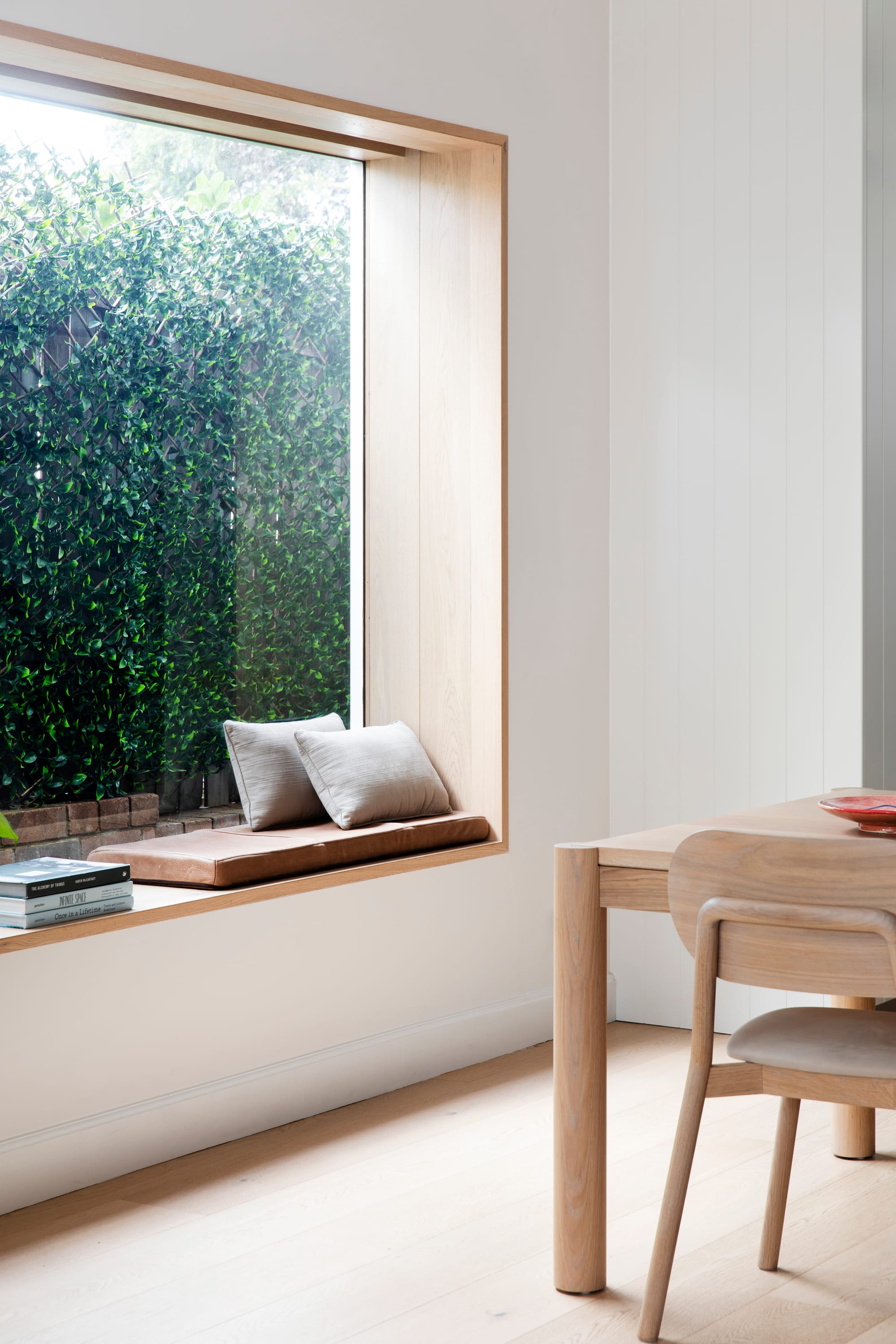 Bondi Beach House by Baikie Corr Architecture. Photography by Chris Warnes. Integrated timber bench seat overlooking garden, in dining room with timer floors, timber table and white walls. 