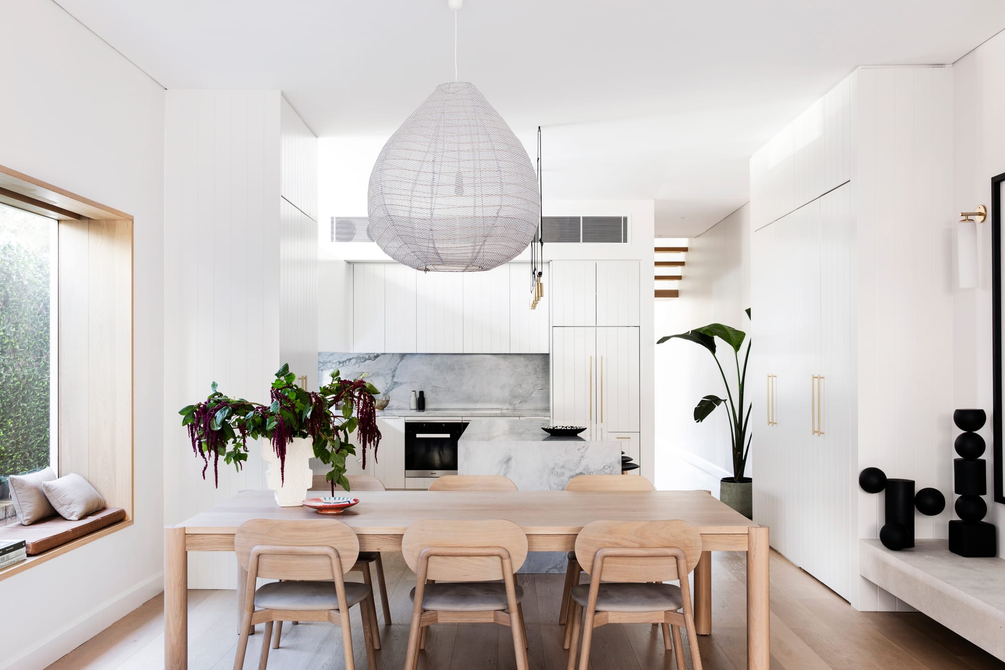 Bondi Beach House by Baikie Corr Architecture. Photography by Chris Warnes. Kitchen and dining space with timber dining table, white cabinetry, sheer pendant and white walls. 