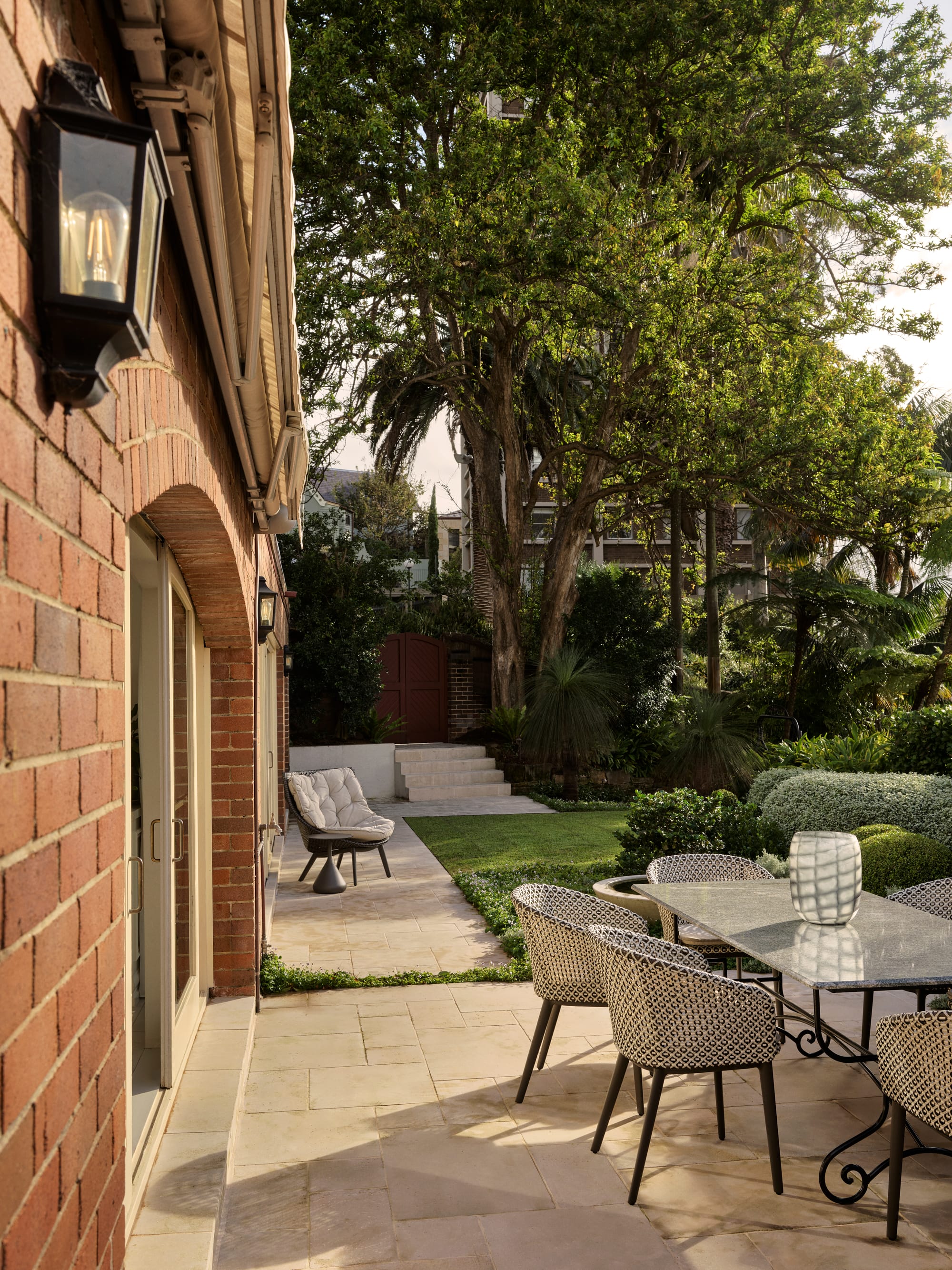 The Darling Edit by Marylou Sobel Interior Design. Photography by Anson Smart. Exterior of home with paved patio with dining table, brick walls and lush gardens. 