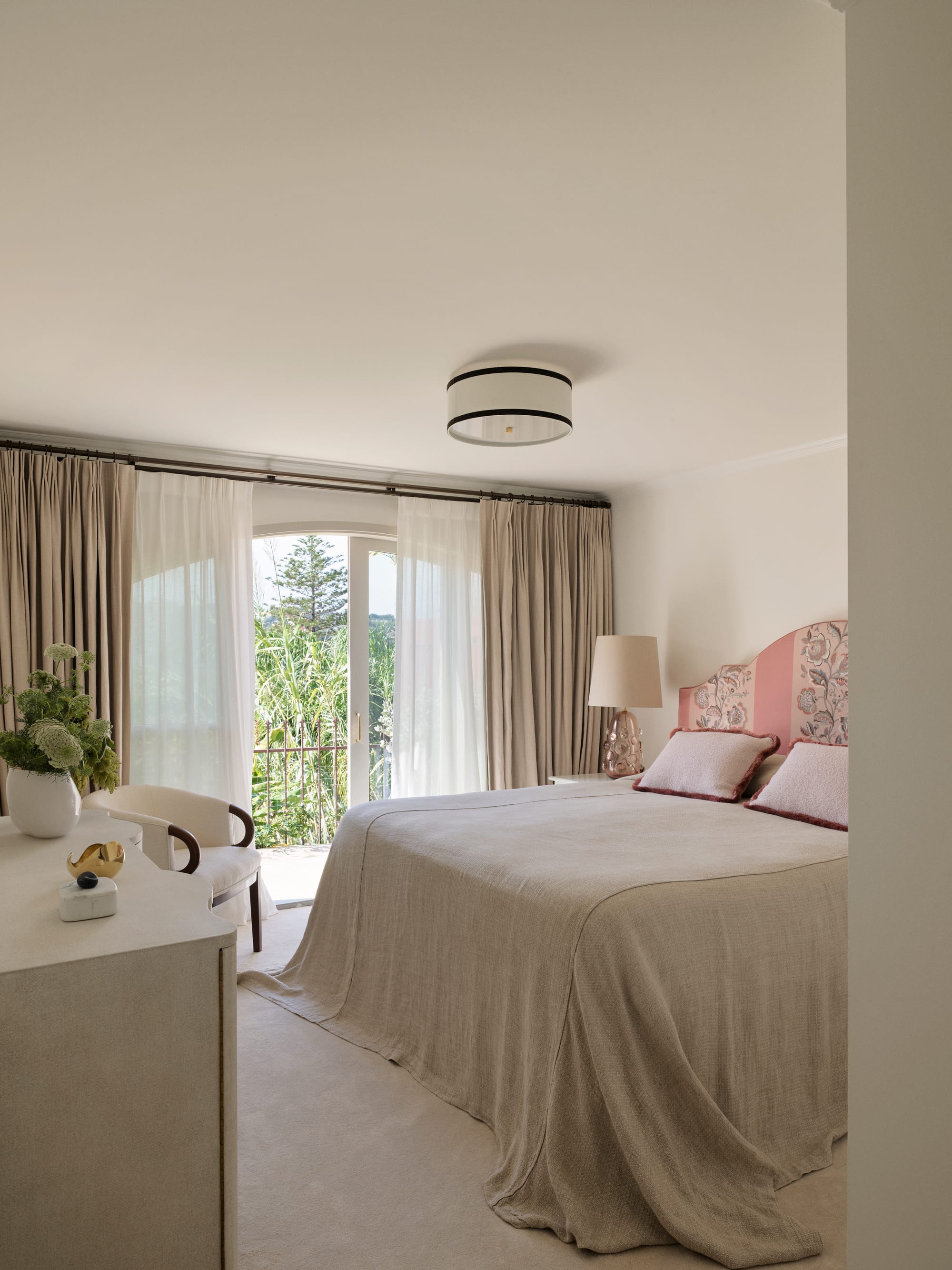 The Darling Edit by Marylou Sobel Interior Design. Photography by Anson Smart. Bedroom with pink patterned fabric headboard, beige linen bedding, light carpets and windows overlooking balcony and gardens. 