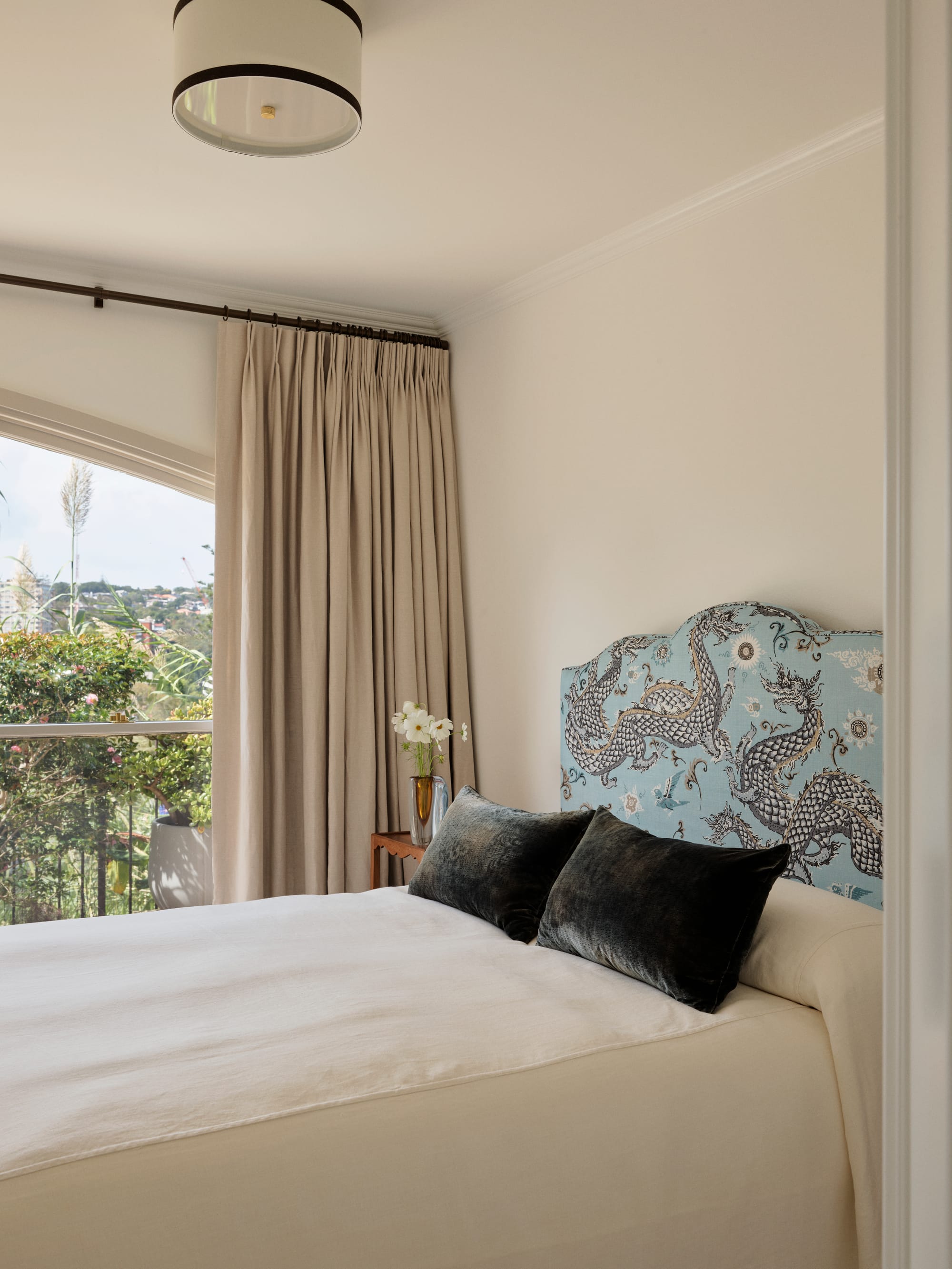 The Darling Edit by Marylou Sobel Interior Design. Photography by Anson Smart. Bedroom with blue patterned fabric headboard, white bedding, navy velvet pillows and beige curtains over windows. 