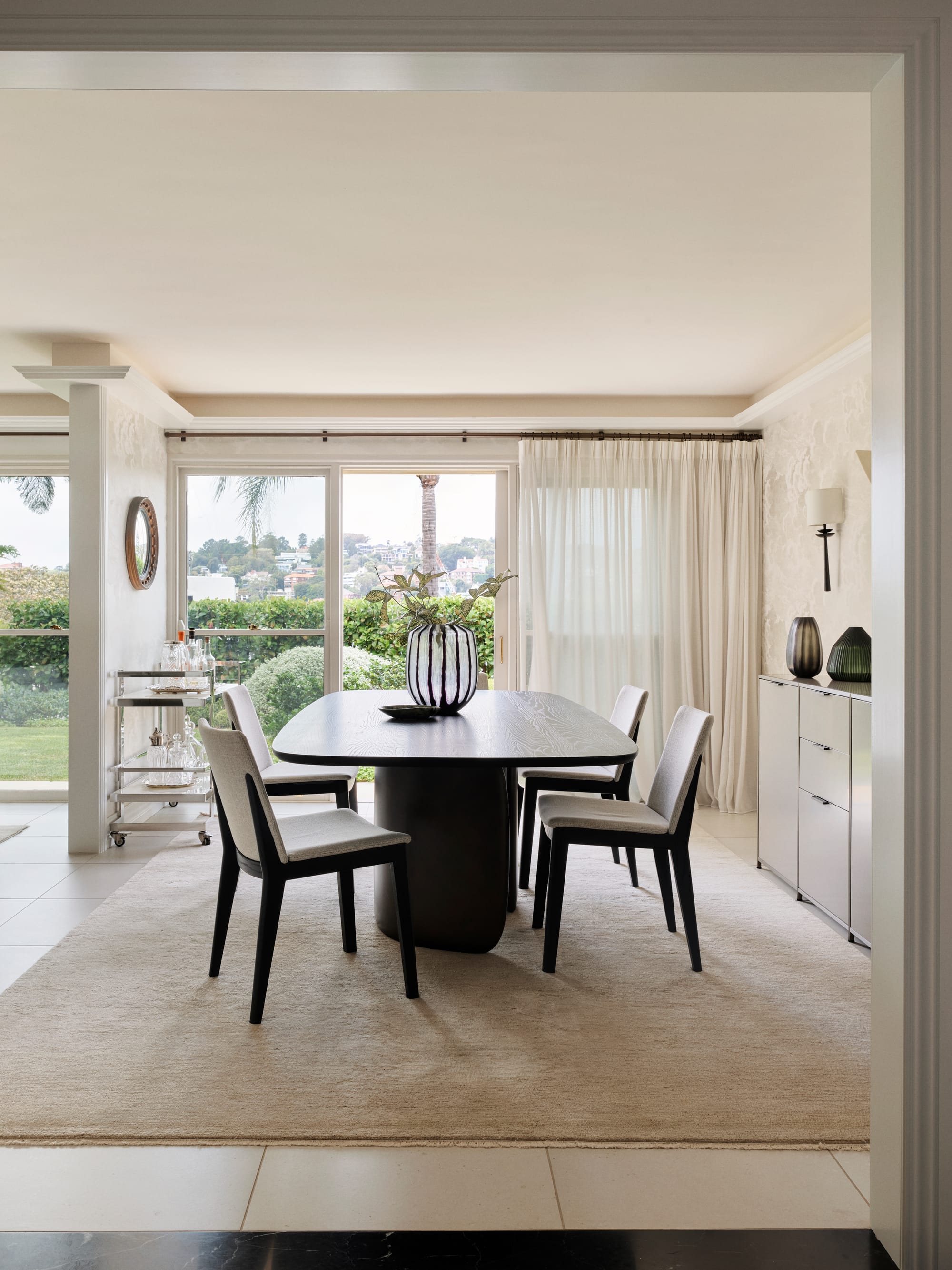 The Darling Edit by Marylou Sobel Interior Design. Photography by Anson Smart. Dining space with carpeted rug, dark timber dining table and chairs, and floor length windows overlooking garden. 