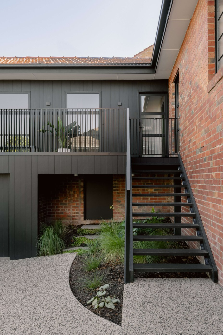 MAUD by Mancini Made. Photography by Elise Scott. Black exterior staircase running alongside red brick wall to second story of black timber clad home.
