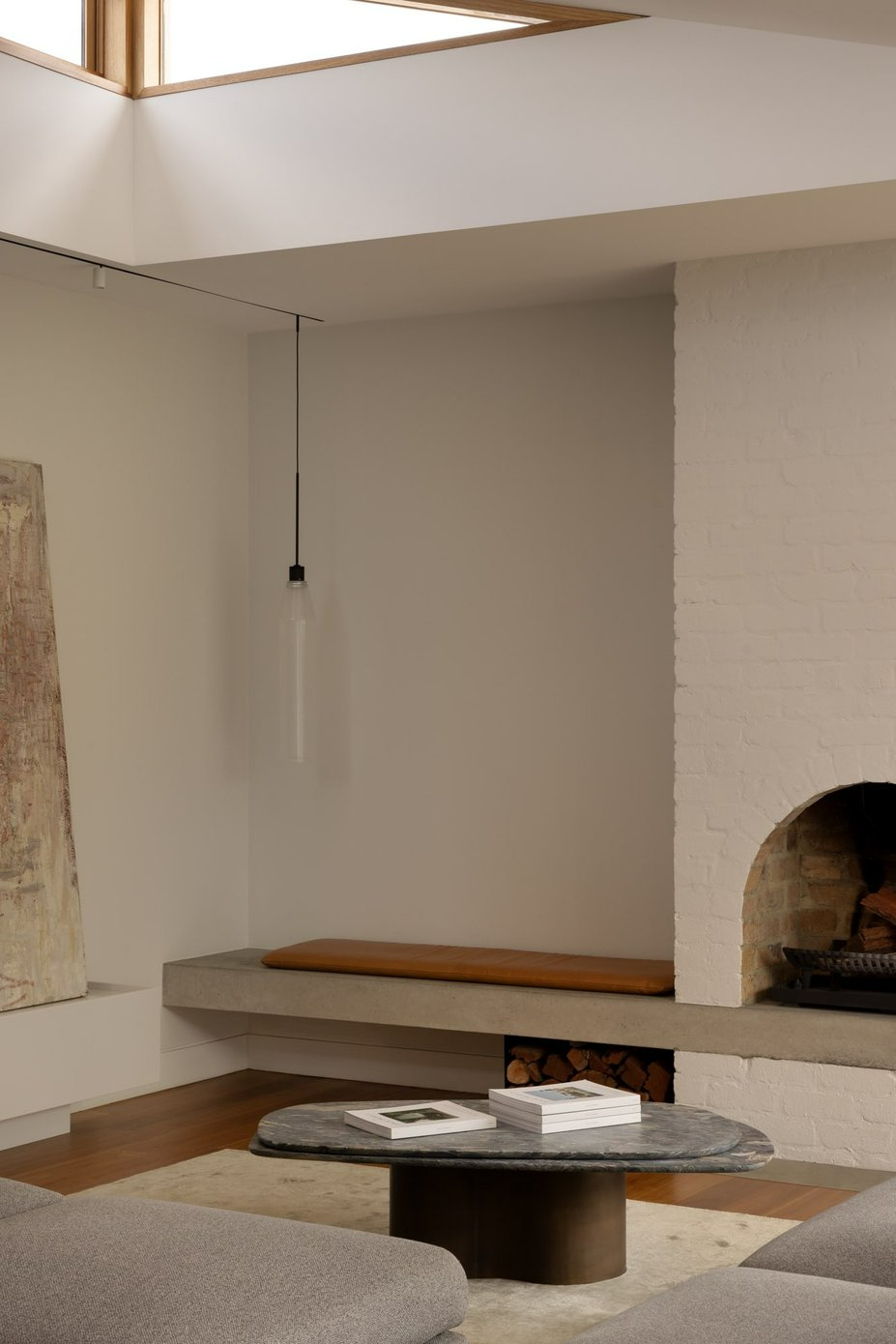 Ormond by Telha Clarke. Photography by Tim Kaye. Interior living space with white brick walls, a concrete floating bench seat, timber floors and grey couches. 