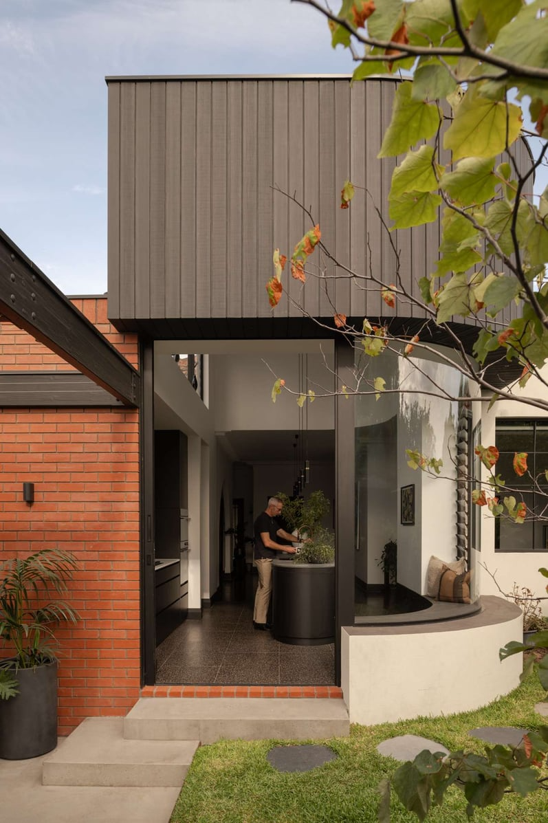 The Alma by &Dalecki. Photography by Dion Robeson. Rear facade of home with curved exterior finished with red brick, white concrete and black framed windows and doors. 
