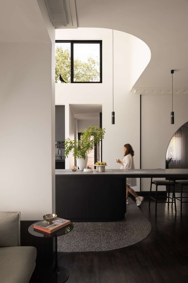 The Alma by &Dalecki. Photography by Dion Robeson. Open plan kitchen and iving space with double height, curved opening and skylight, black timber floors and black cabinetry. 