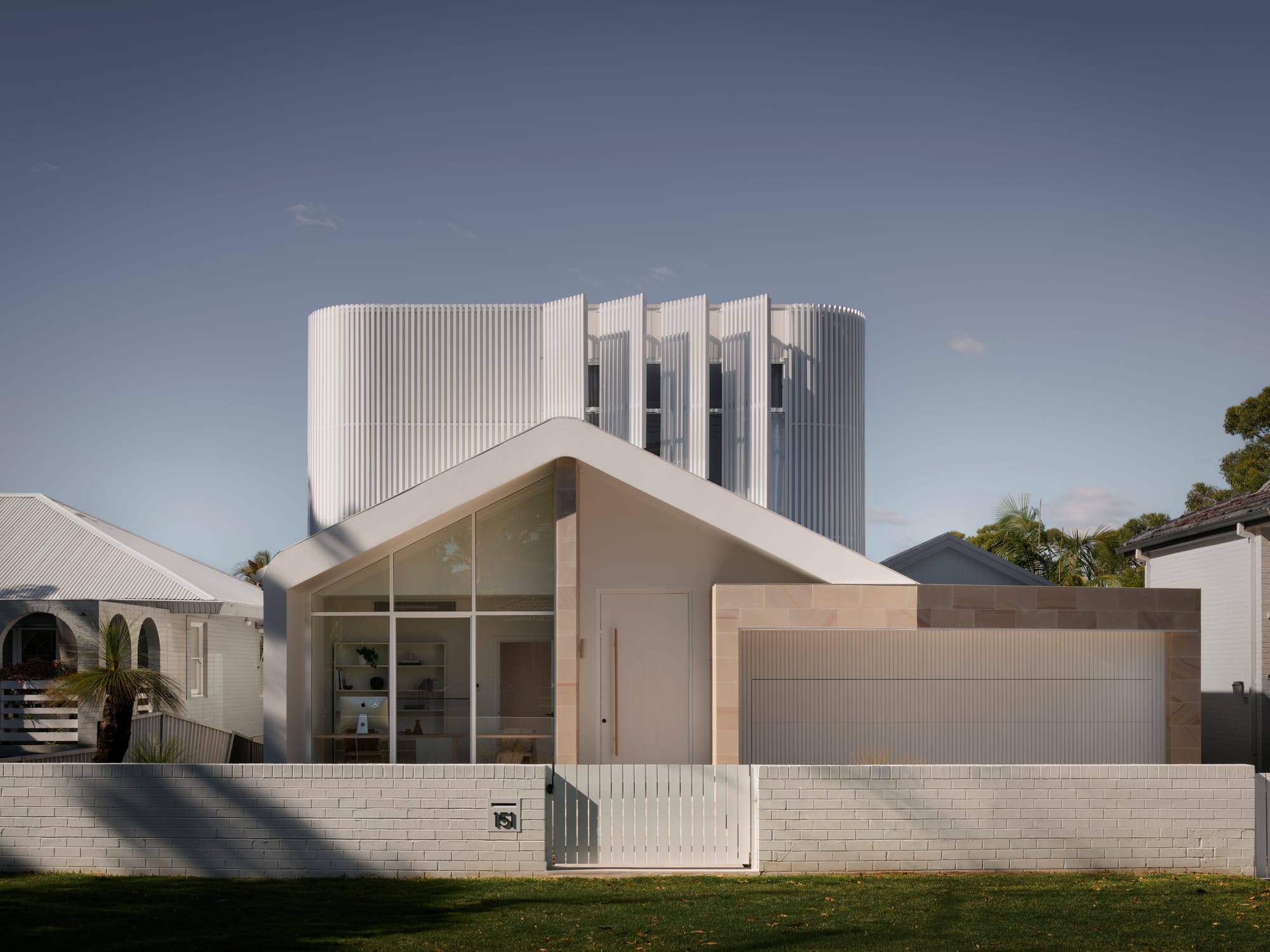 Sienna House by 868 Architects. Photography by Luke Butterly. Front facade of double storey contemporary home with white brick fence, white pitched roof and white timber clad upper level. 