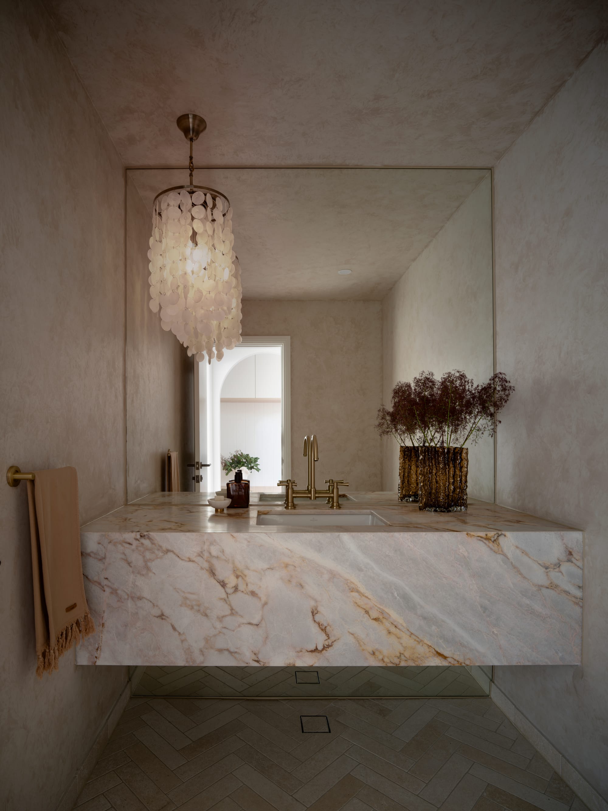 Sienna House by 868 Architects. Photography by Luke Butterly. Bathroom with herringbone tiled floors, heavily-veined counter, mirrored splashback and lime-washed walls. 