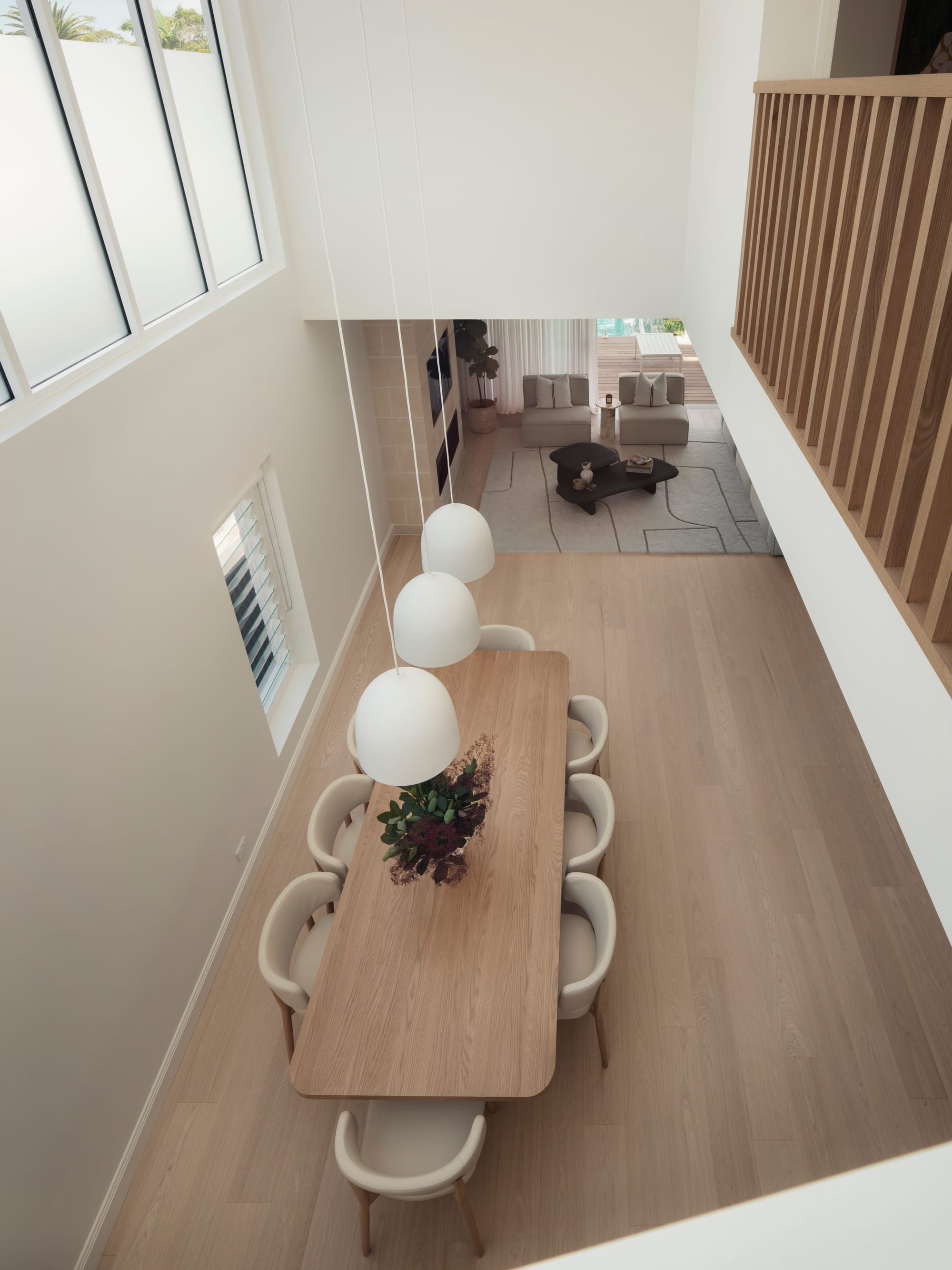 Sienna House by 868 Architects. Photography by Luke Butterly. Birds-eye-view of timber dining table in open plan space with timber flooring and white walls, from upper-level void. 