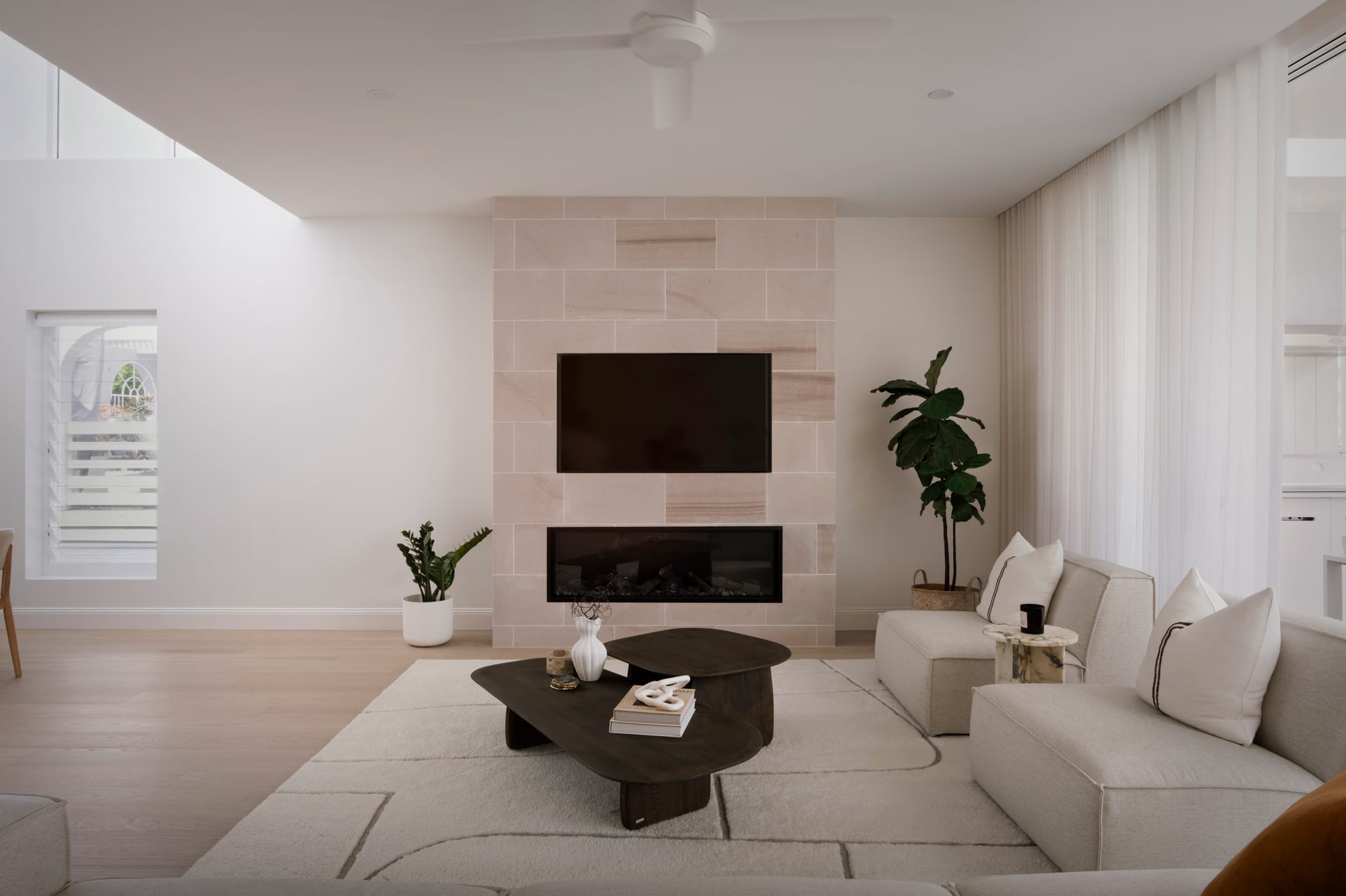Sienna House by 868 Architects. Photography by Luke Butterly. Open plan living space with timber flooring, sandstone-clad integrated fireplace, white couch and rug, and black coffee table. 