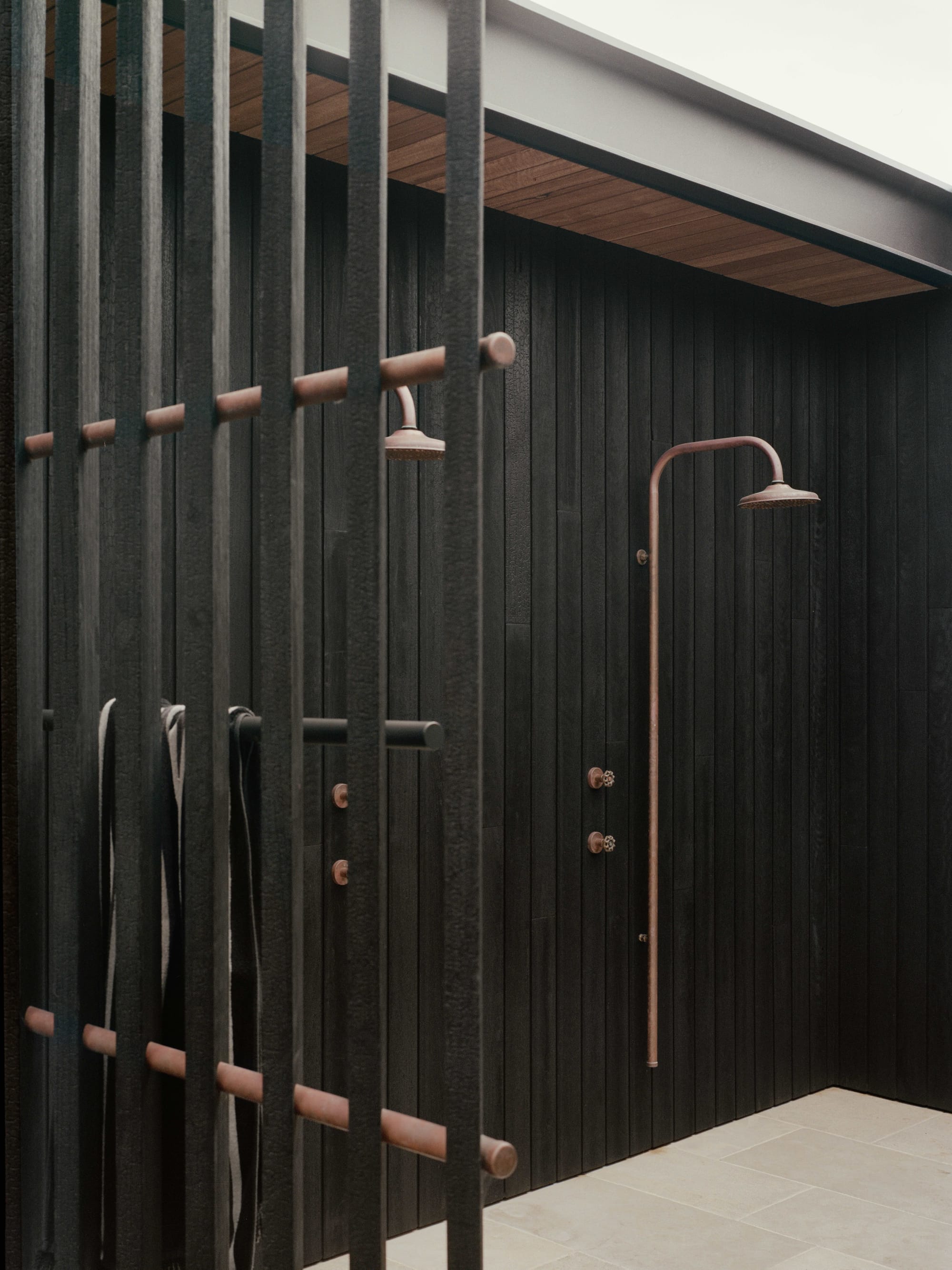 Anglesea House by Eckersley Architects. Photography by Tasha Tylee. Exterior shower in recess with charcoal timber cladding, stone flooring and brass fixtures. 