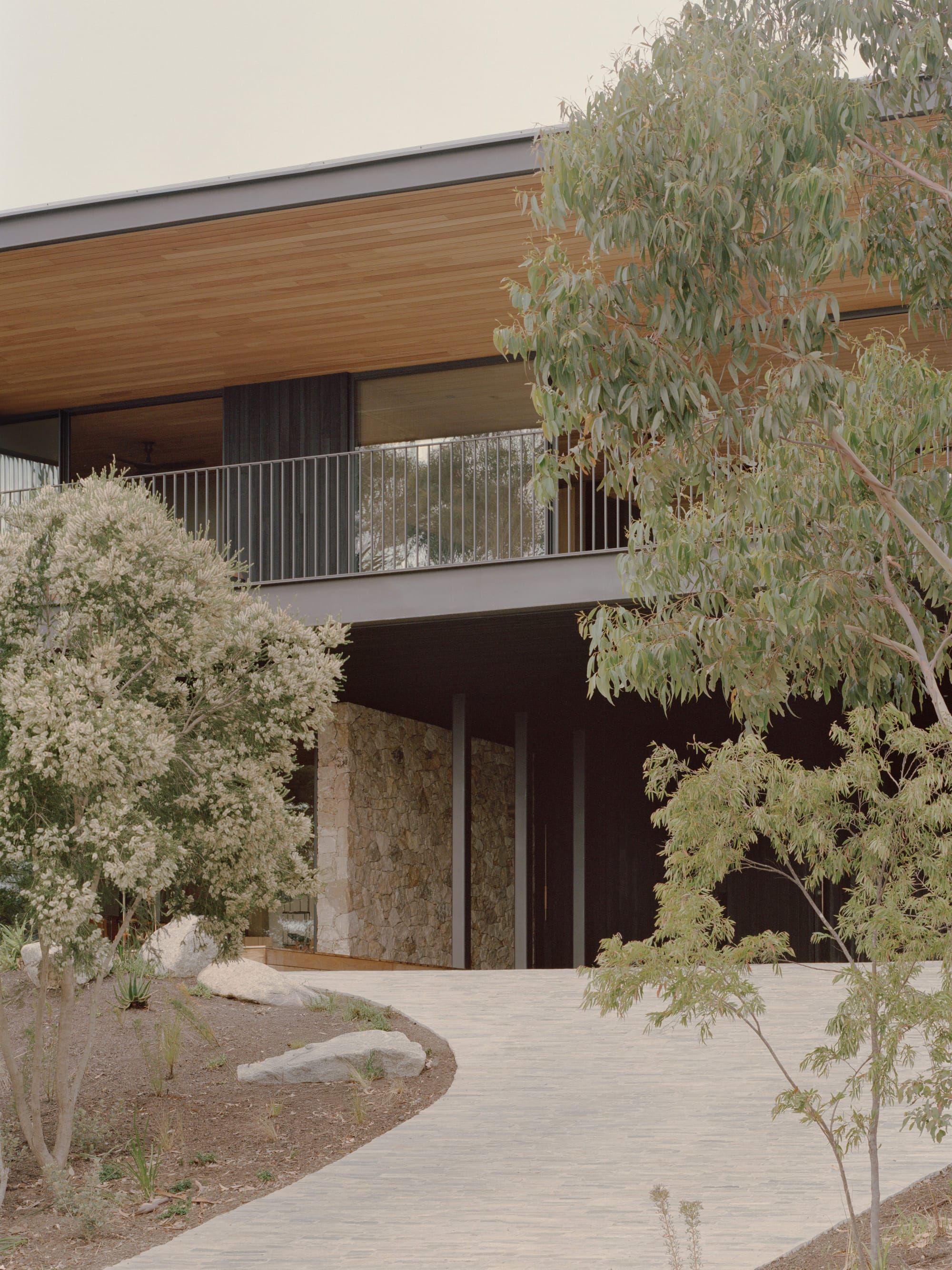 Anglesea House by Eckersley Architects. Photography by Tasha Tylee. Front facade of double storey contemporary home with black timber accents, stone walls, and light timber clad ceilings. 