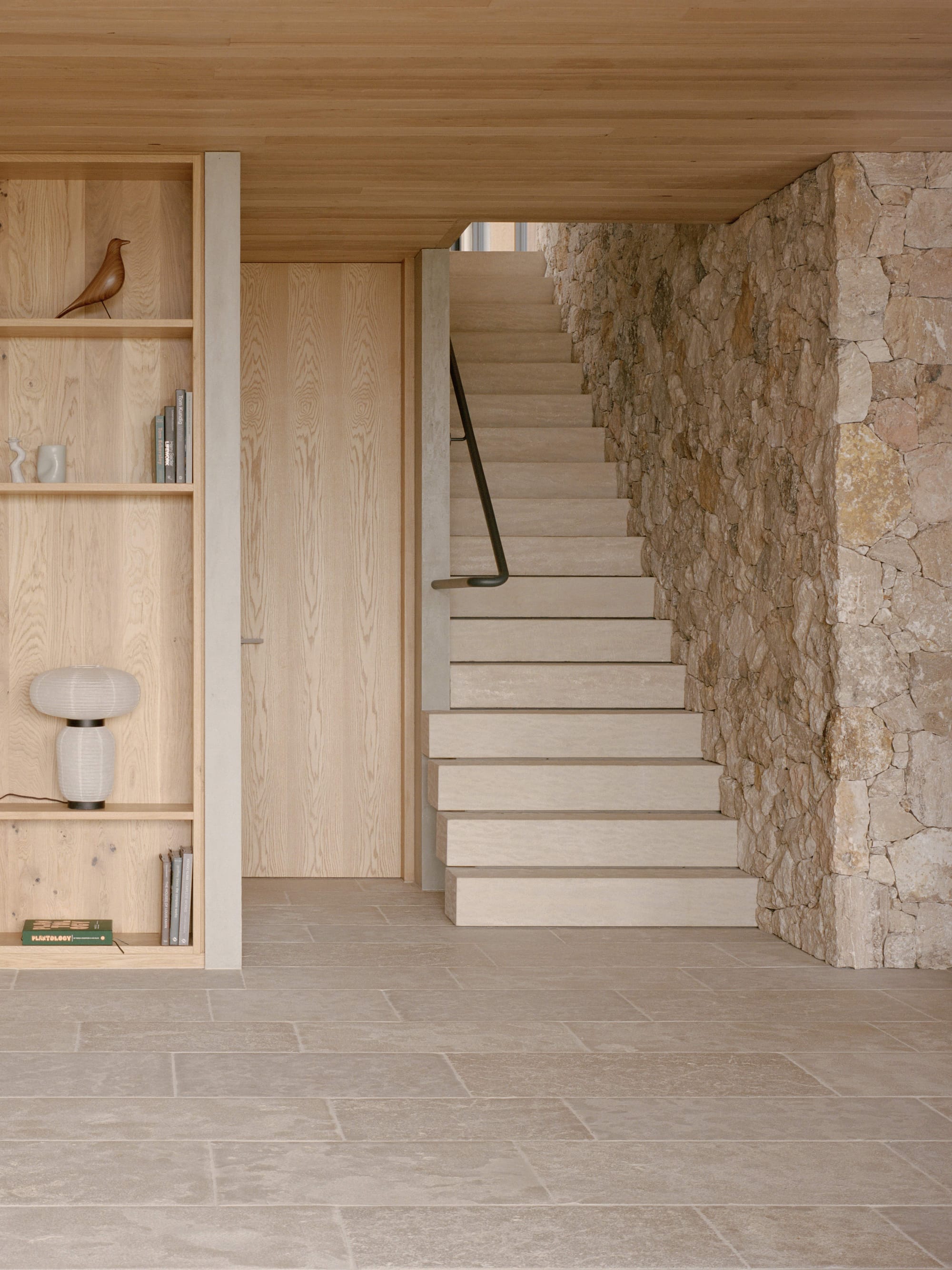 Anglesea House by Eckersley Architects. Photography by Tasha Tylee. Interior timber staircase running alongside packed stone wall with stone flooring and integrate timber storage. 