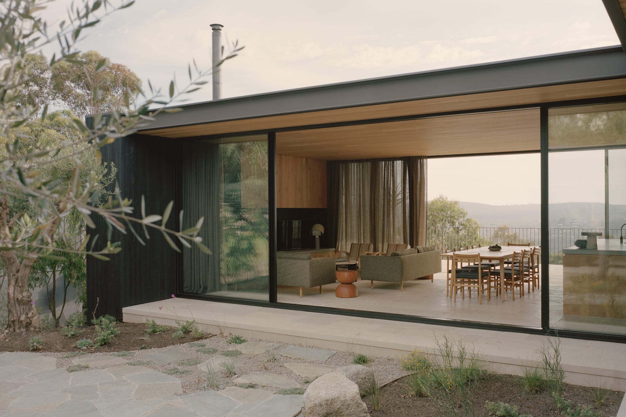Anglesea House by Eckersley Architects. Photography by Tasha Tylee. Exterior facade of home showcasing open plan living, kitchen and dining room interior layout through full-height glass walls. 