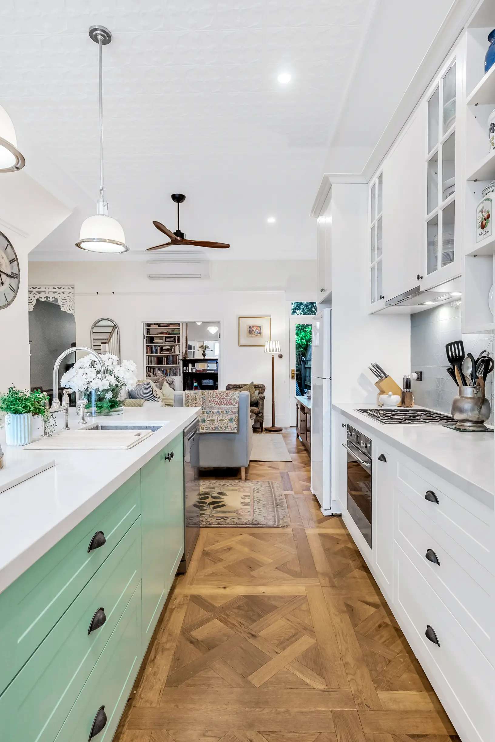 Vibrant Charm by Emotive Designs. Kitchen with parquet timber flooring and teal and white cabinetry 
