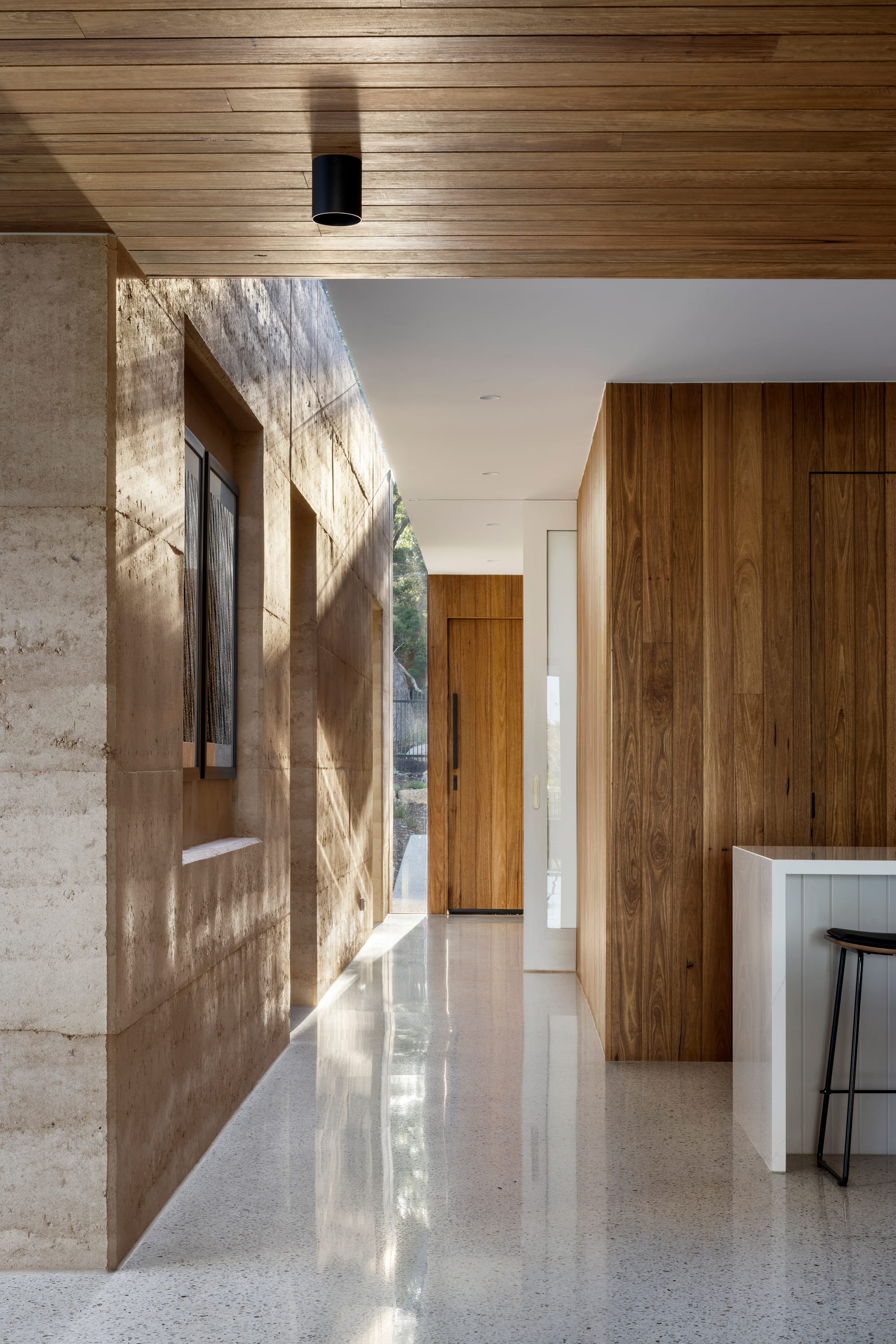 Earth + Sky House by Kirsten Johnstone Architecture. Photography by Tatjana Plitt. Entry and open plan kitchen with polished concrete flooring, and rammed earth and timber clad walls. 