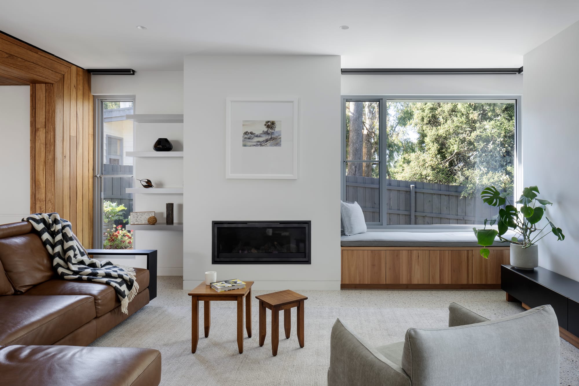 Earth + Sky House by Kirsten Johnstone Architecture. Photography by Tatjana Plitt. Living space with fireplace, integrated timber bench window seating, grey carpets, white walls and brown leather couch. 