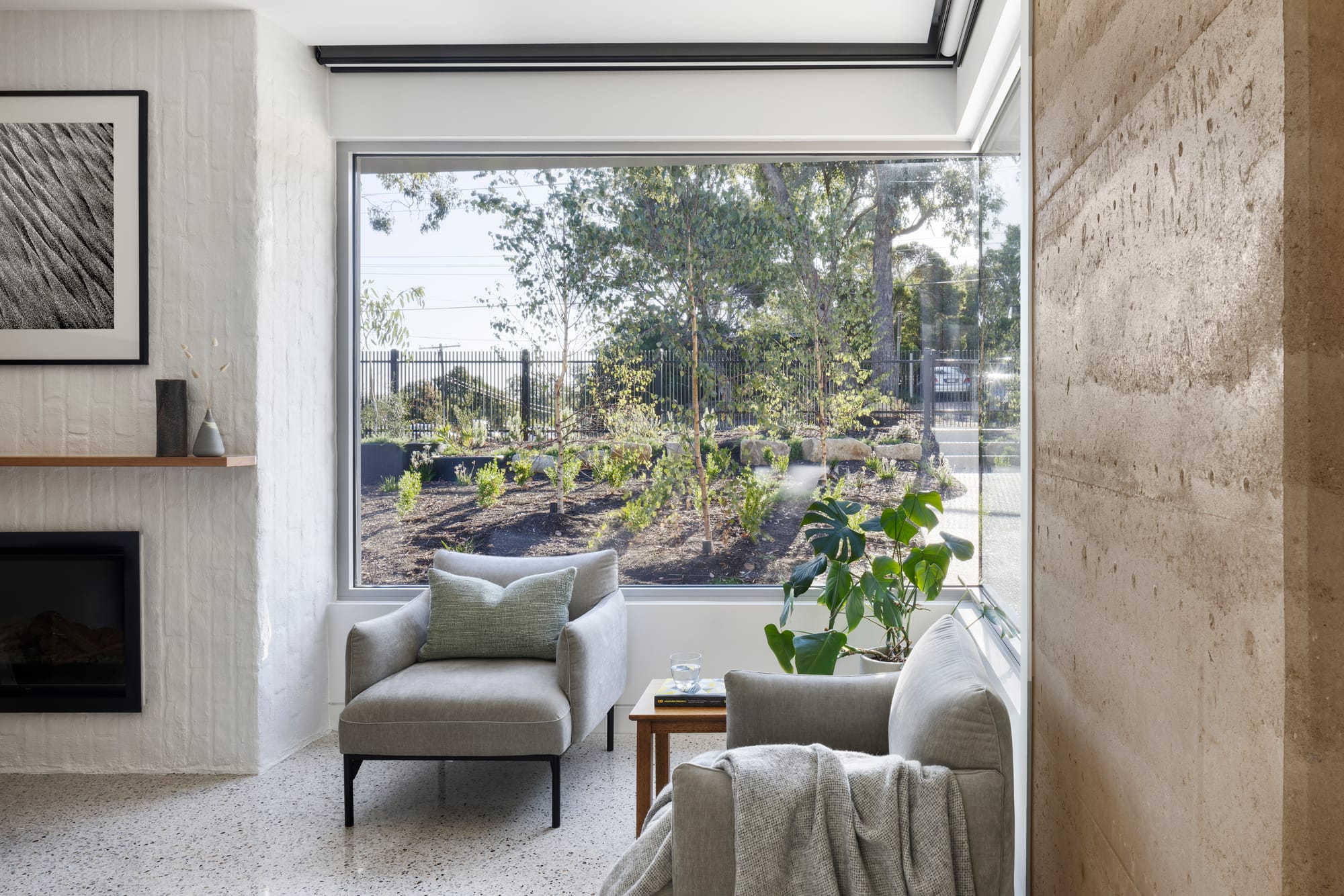 Earth + Sky House by Kirsten Johnstone Architecture. Photography by Tatjana Plitt. Living room with polished concrete floors, rammed earth and painted white brick walls, large corner window and grey armchairs. 