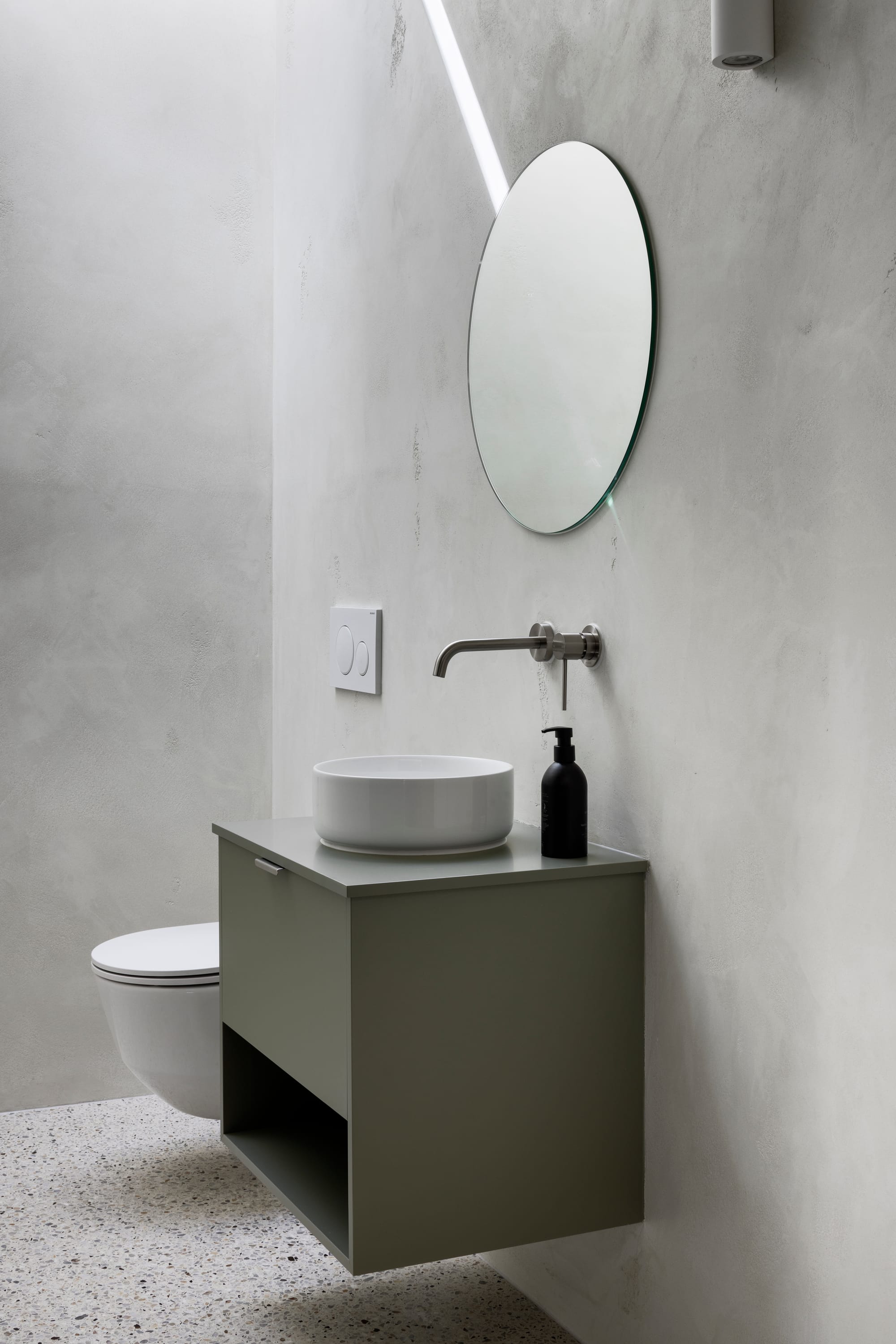 Earth + Sky House by Kirsten Johnstone Architecture. Photography by Tatjana Plitt. Minimalistic bathroom with limewashed grey walls, floating grey cabinet with raised circular sink, floating white toilet and polished concrete floors. 