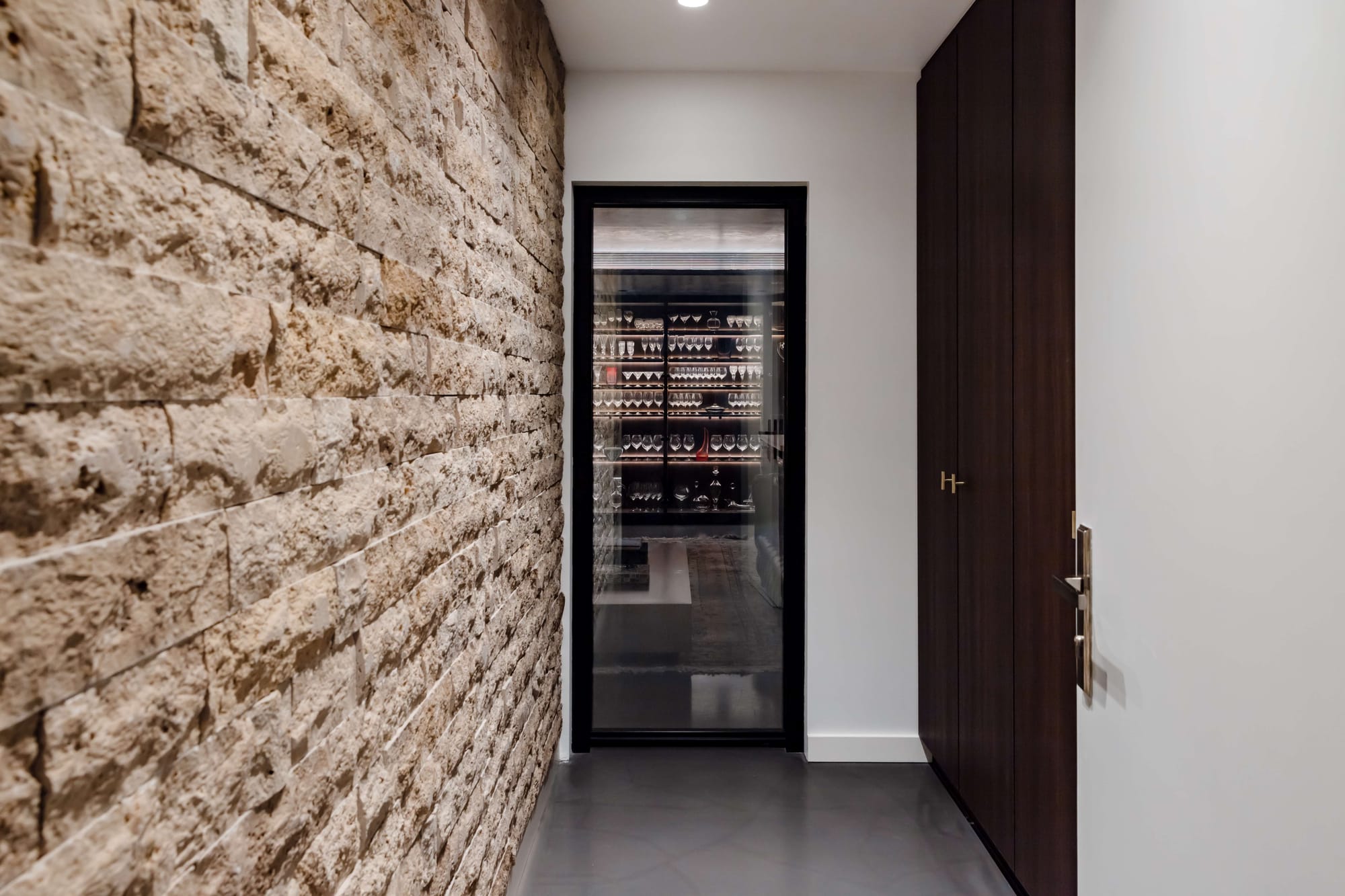 Avalon Beach Wine Cellar & Lounge by Nx Studio. Photography by REM Design House. Stone wall in white hallway leading to black and glass cellar door. 