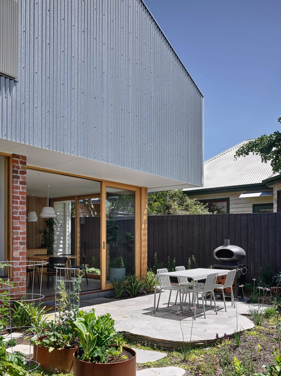 Brooke by Ola Architecture Studio. Photography by Derek Swalwell. Garden with stone patio, white dining table and exterior facade of home finished with aluminum sheeting. 
