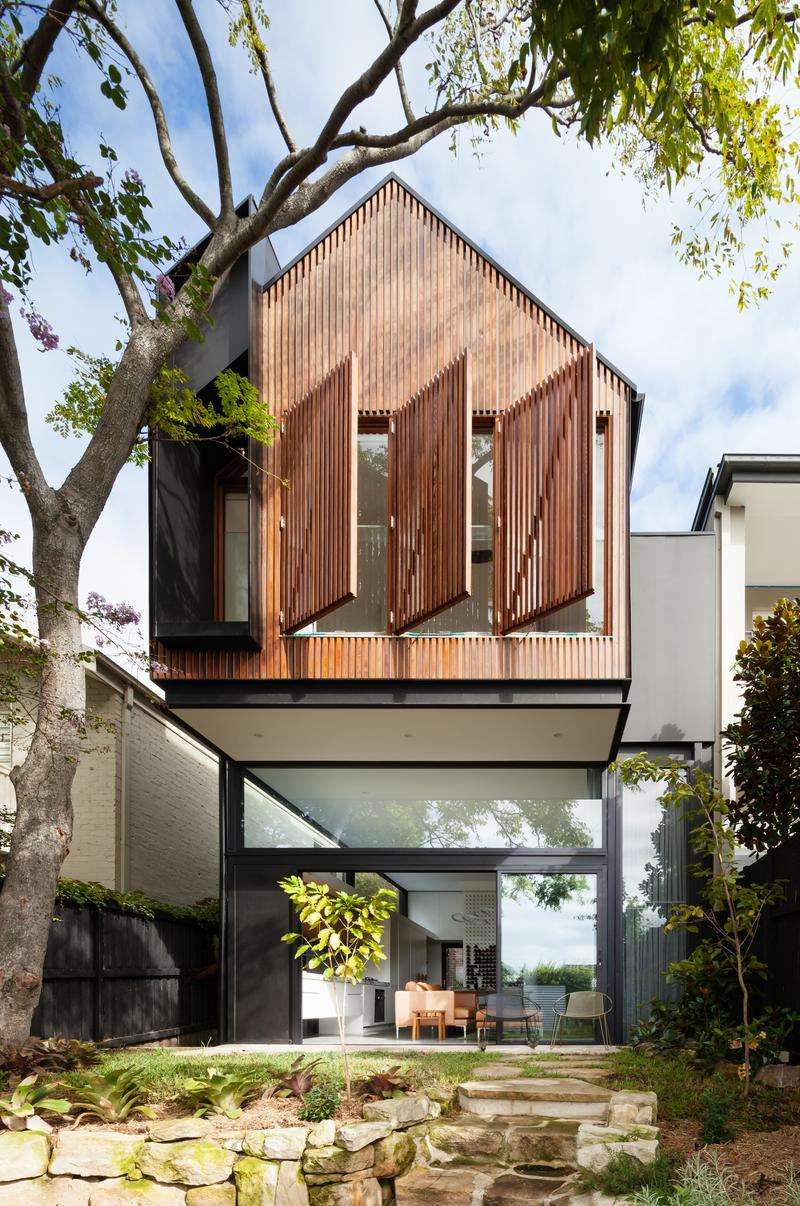 Randwick by Matt Day Architect. Photography by Katherine Lui. Rear facade of double storey home with pitched, timber clad second storey, garden with stone retaining walls and black sliding doors. 