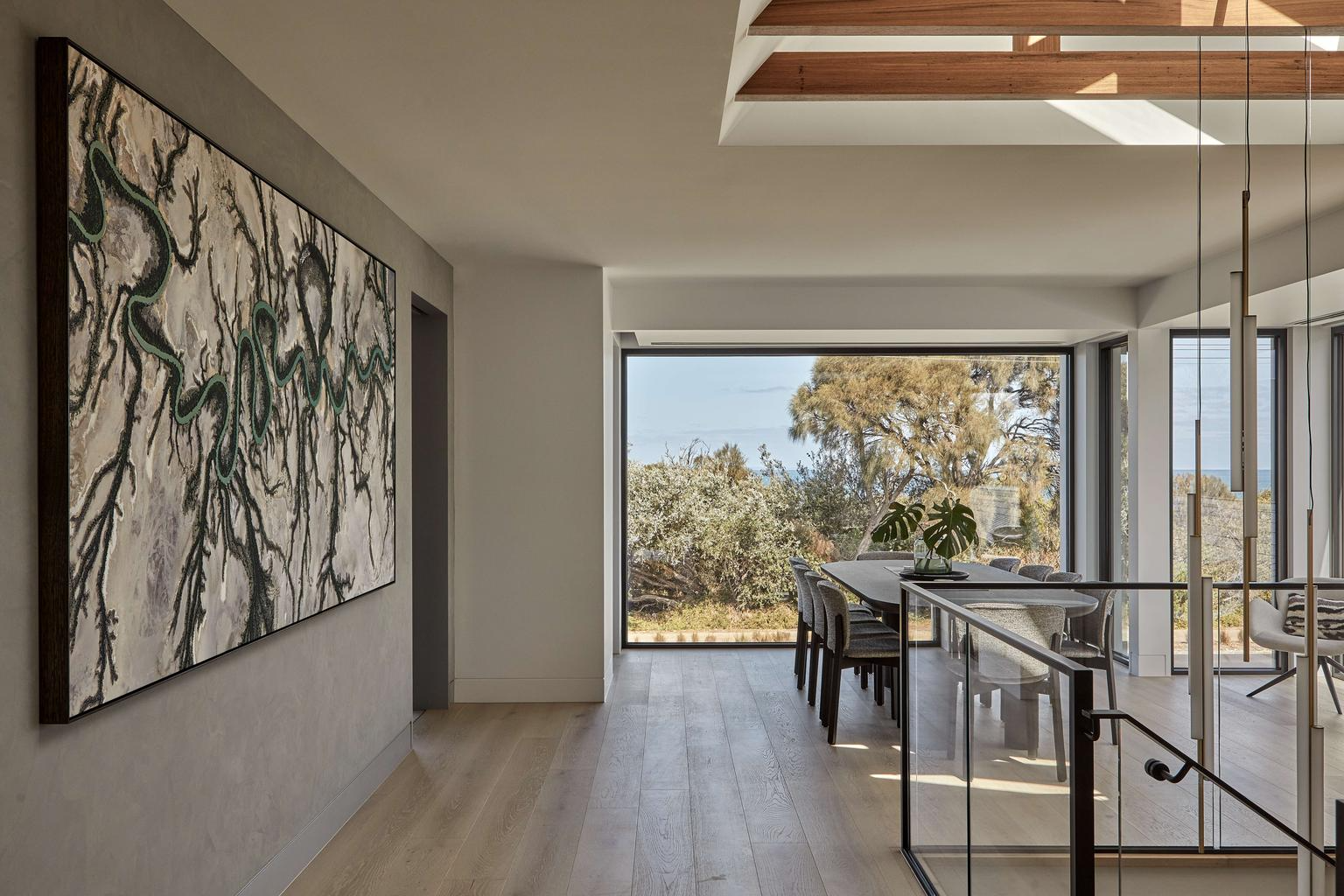 Horizon Home by Samuel Architecture. Photography by Dave Kulesza. Open plan hallway and dining space with large abstract wall art, glass balustrade and large windows with landscape views. 