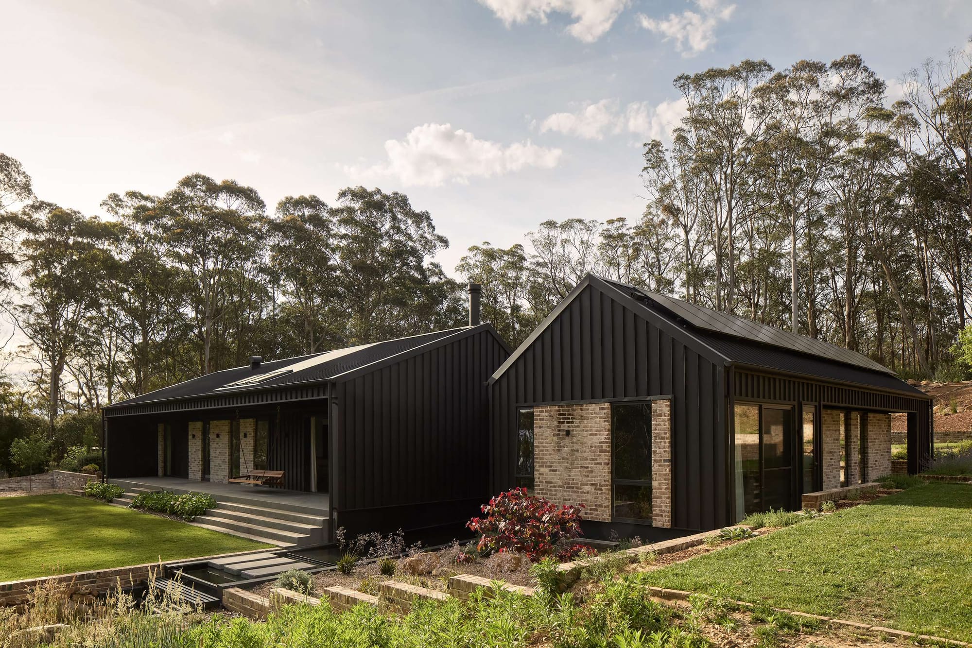 House Kimberley by AO Design Studio. Photography by Luc Remond. Two pavilion style homes with black clad exterior, multi-level gardens connected by gardens and concrete steps and grassed areas. 
