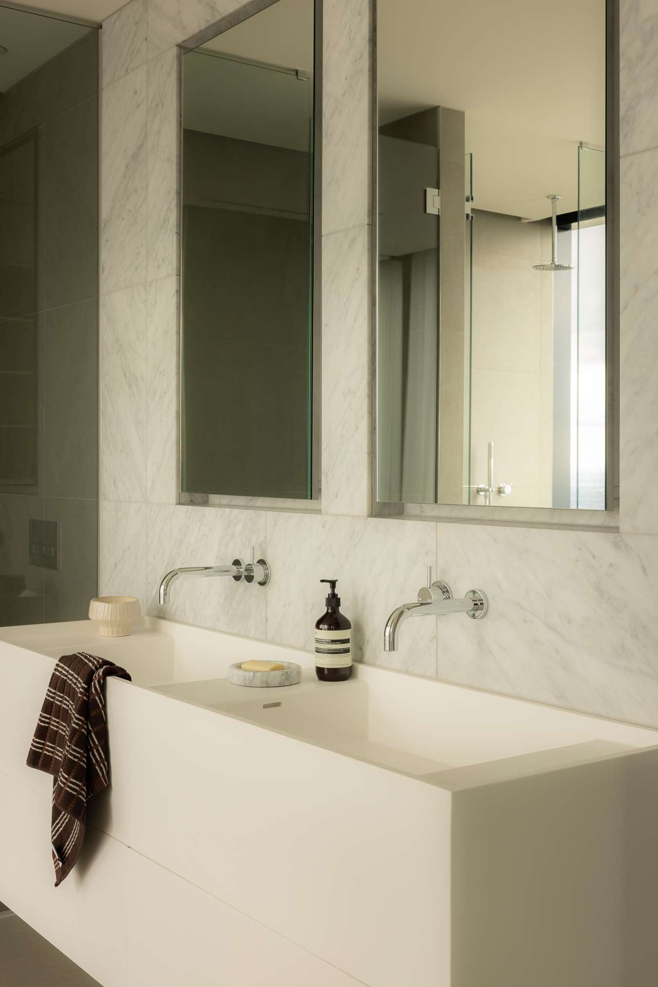 Cloud Residence by FURNISHD. Photography by Dylan James. White double bathroom sink with chrome tapware, recessed wall mirrors, and white marble splashback. 