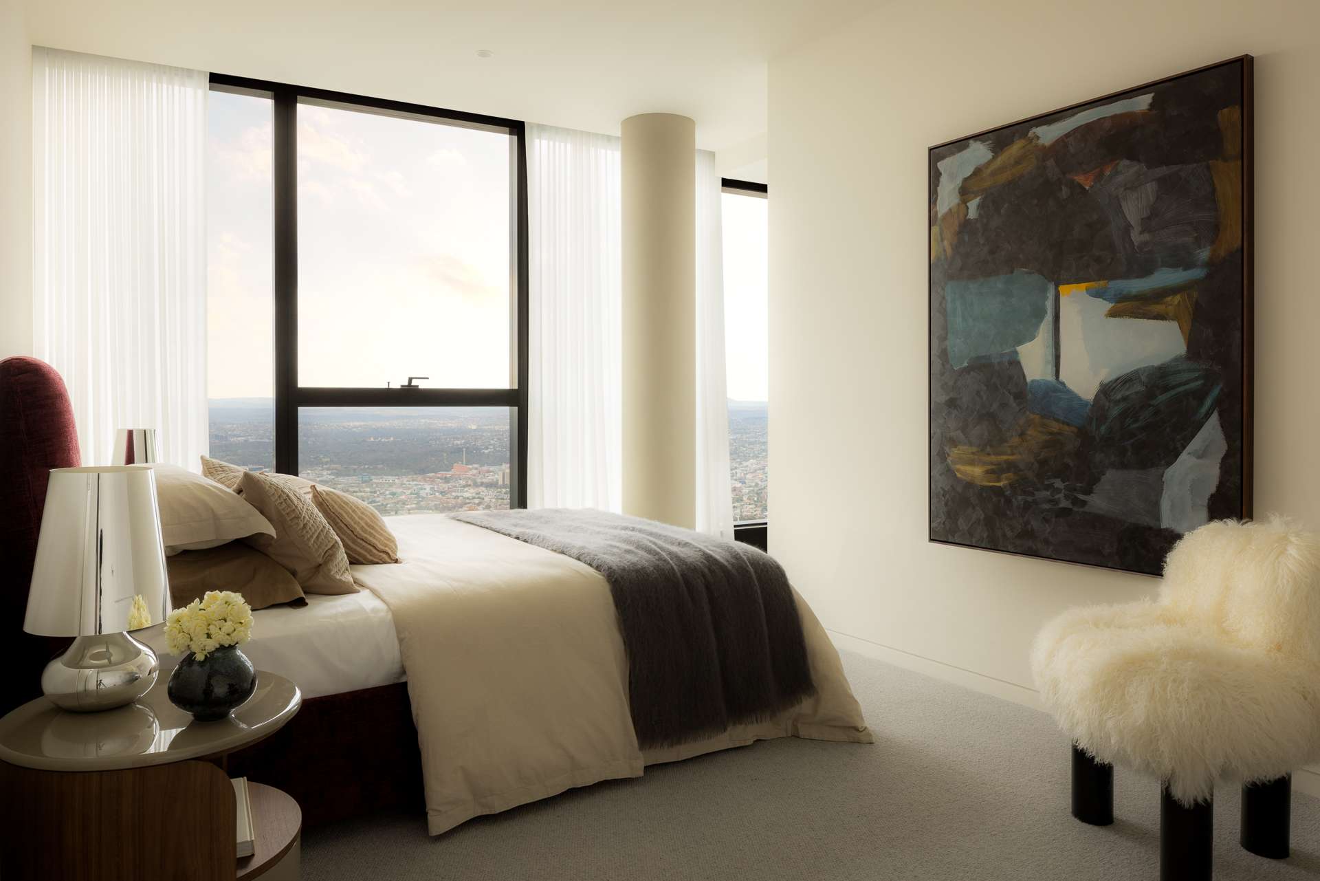 Cloud Residence by FURNISHD. Photography by Dylan James. Bedroom with white walls, abstract wall art, fluffy white armchair and full height glass windows with city views. 