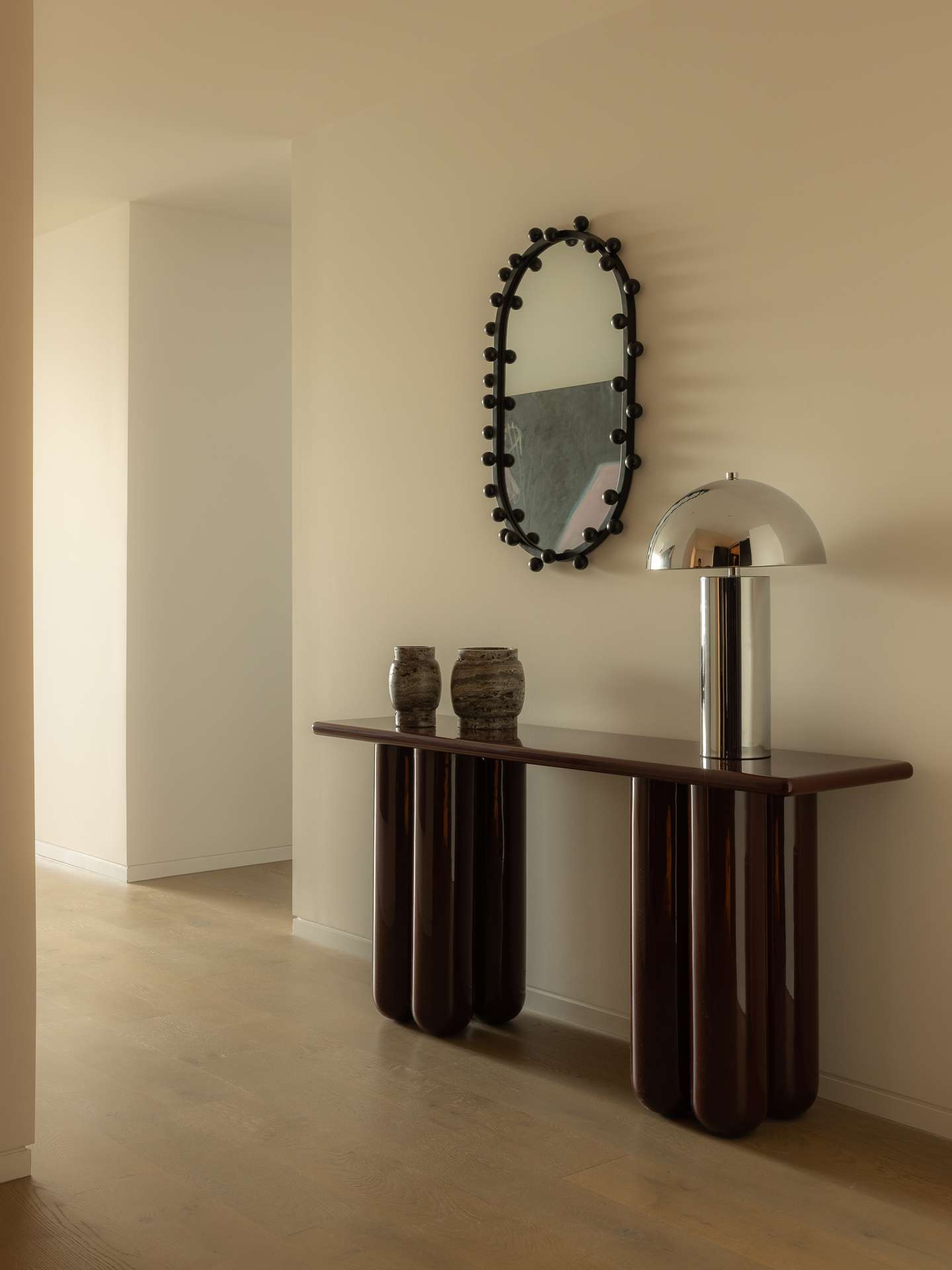 Cloud Residence by FURNISHD. Photography by Dylan James. Hallway with light timber floors, white walls, abstract black wall mirror, and sculptural chocolate brown sideboard with chrome lamp.  