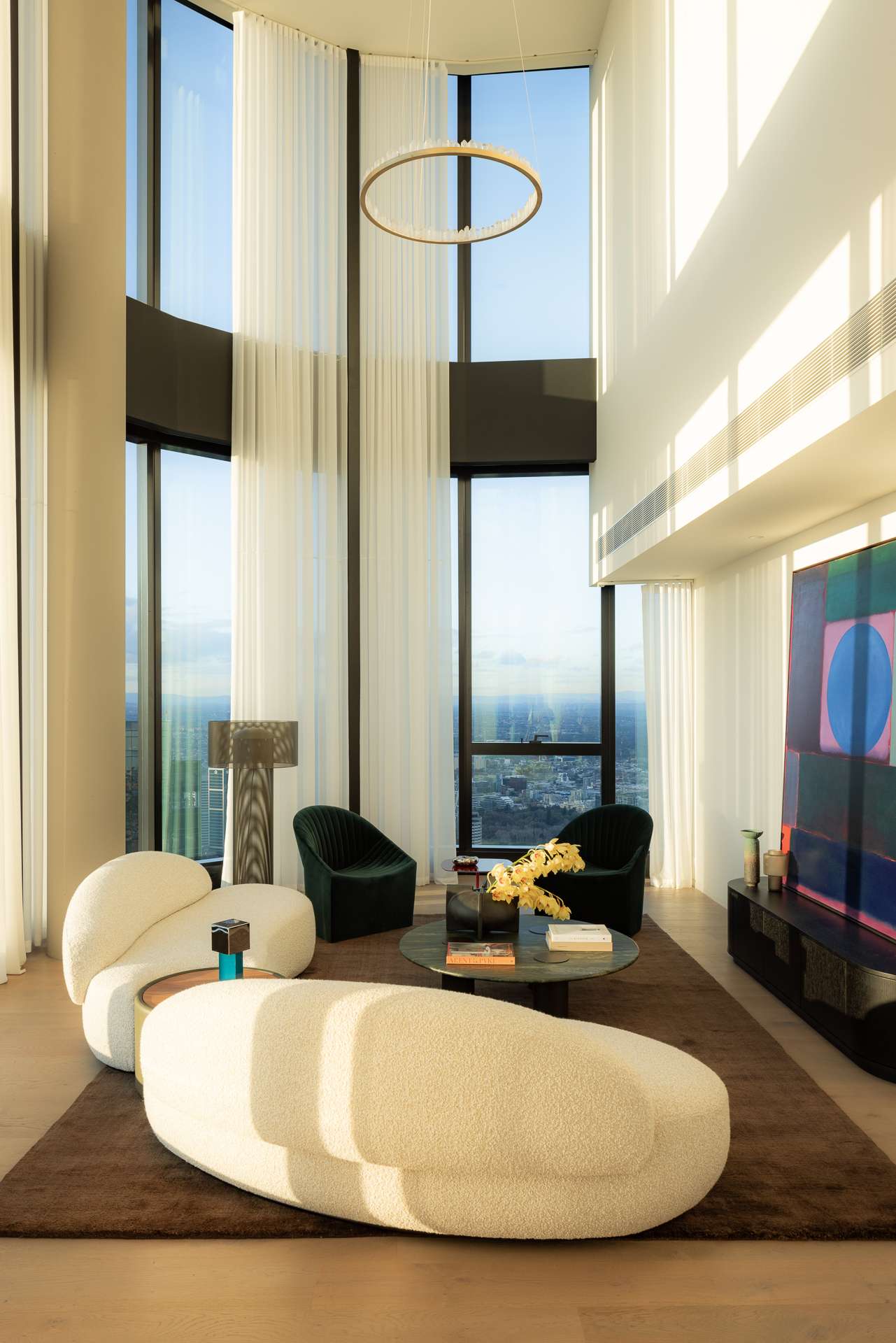 Cloud Residence by FURNISHD. Photography by Dylan James. Living space with boucle white lounges, brown rug and full height glass windows overlooking city. 