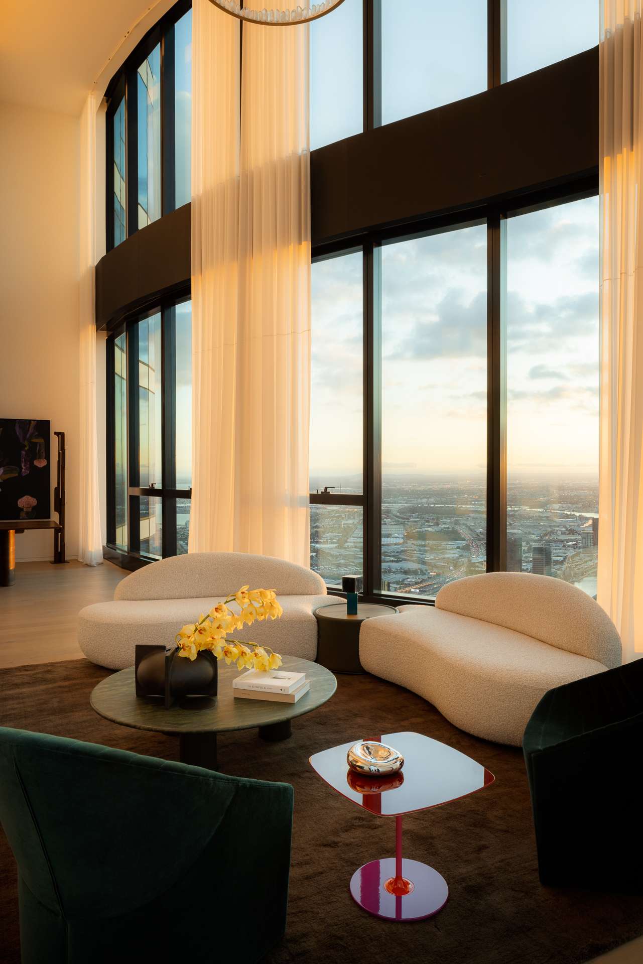 Cloud Residence by FURNISHD. Photography by Dylan James. Living room with full height glass windows, white sheers, white boucle couches, hot pink Perspex side table, jade stone coffee table, and brown rug. 