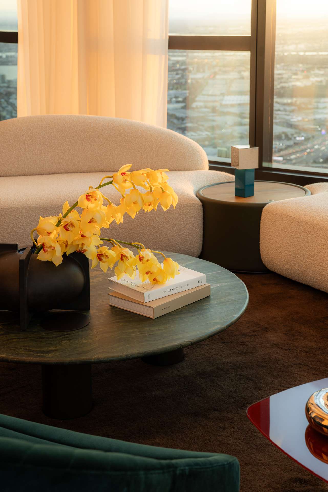 Cloud Residence by FURNISHD. Photography by Dylan James. Round jade stone coffee table with yellow floral arrangement, positioned on chocolate brown floor rug, in front of white boucle couches. 