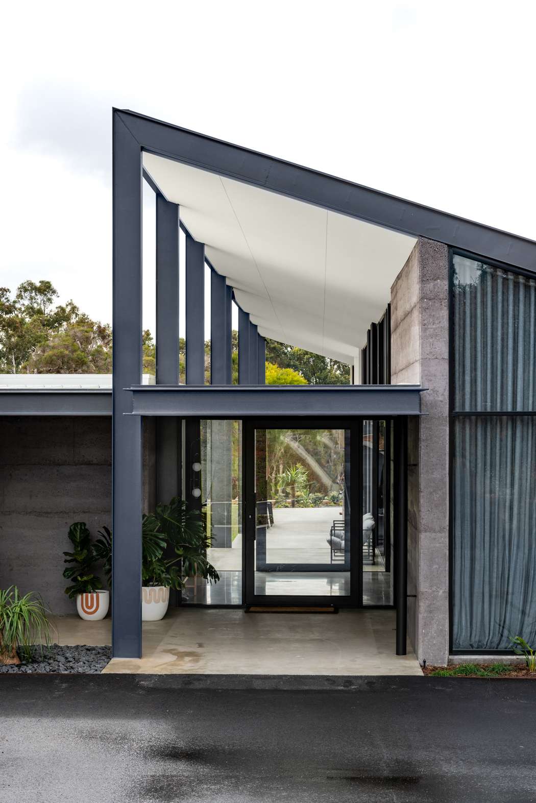 Hausen Court by Keen Architecture. Photography by Keen Architecture. Front facade of home with exposed black steel pillars, concrete walls and glass door. 